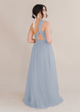 A woman wearing a dusty blue bridesmaid dress with one shoulder strap on a white background by TH&TH Bridesmaids.