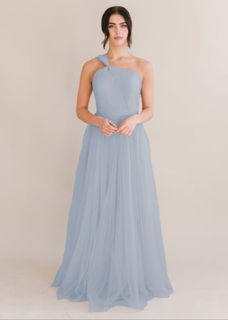 A woman wearing a dusty blue bridesmaid dress with one shoulder strap on a white background by TH&TH Bridesmaids.