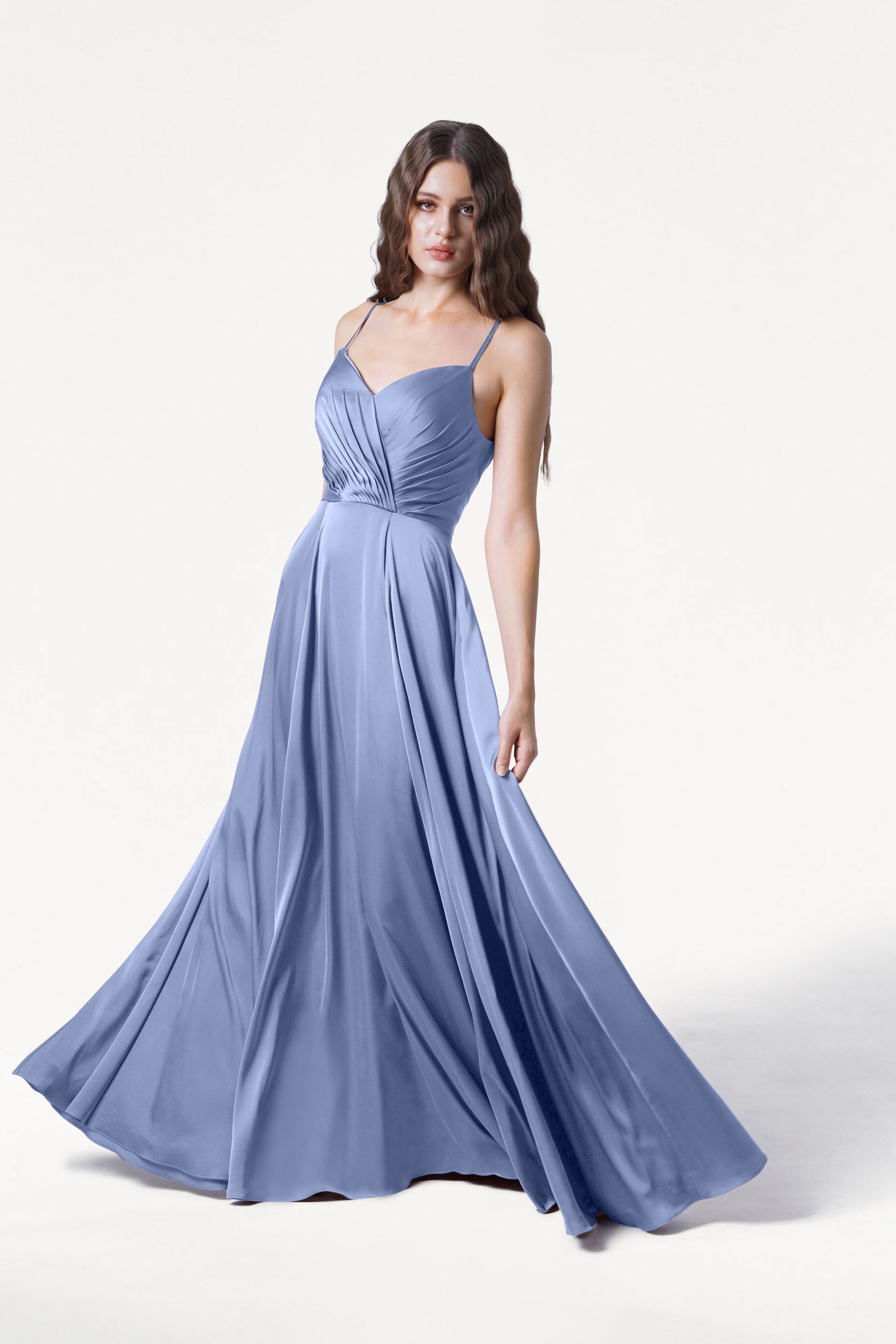A woman models the TH&TH Isla Bridesmaid Dress in French Blue Satin, featuring a pleated bodice and spaghetti straps, standing against a plain white background.