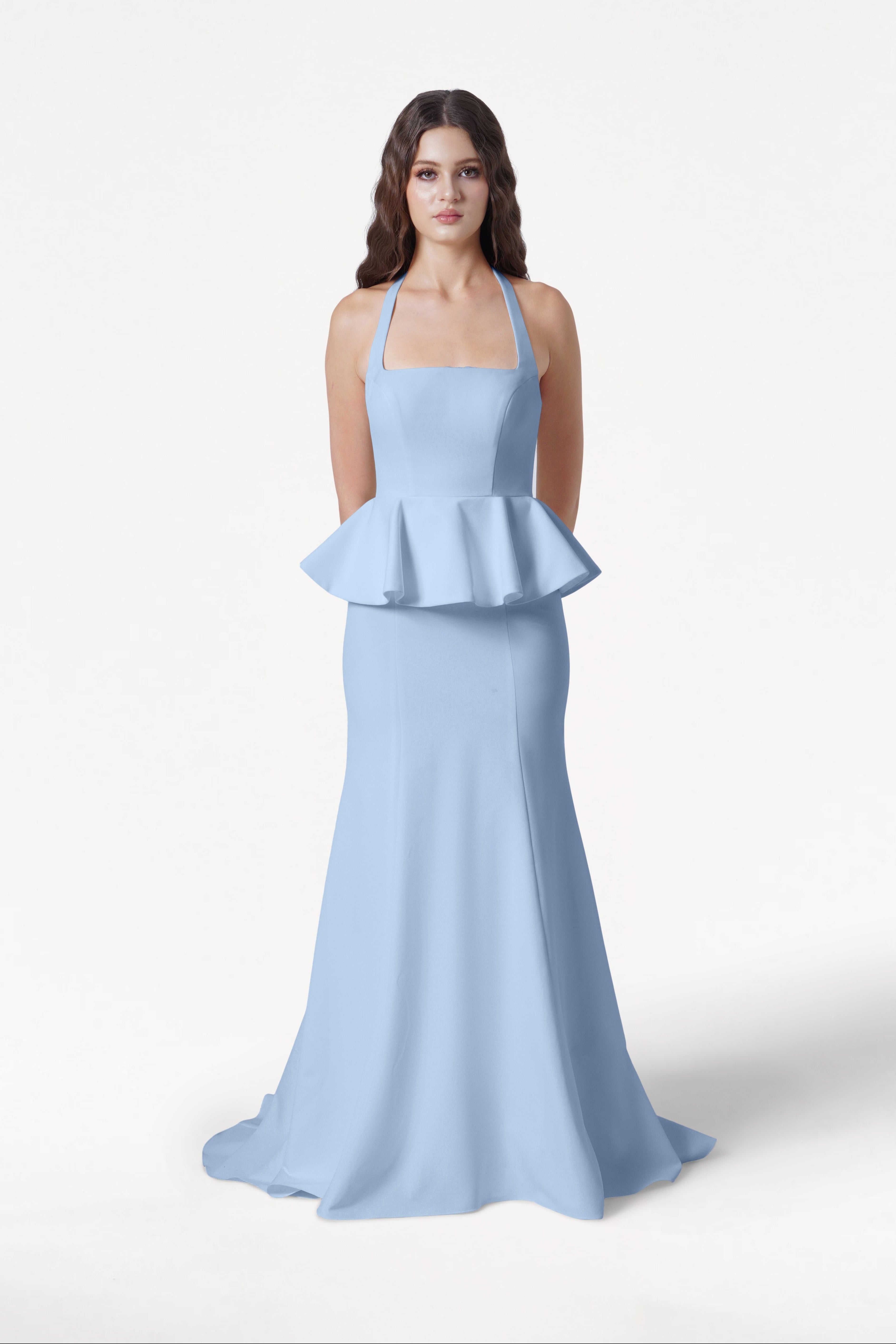 A woman faces forward against a white background, wearing the TH&TH Peony Bridesmaid Dress in Dusty Blue—a floor-length moss crepe gown with a halter neckline and peplum waist detail.