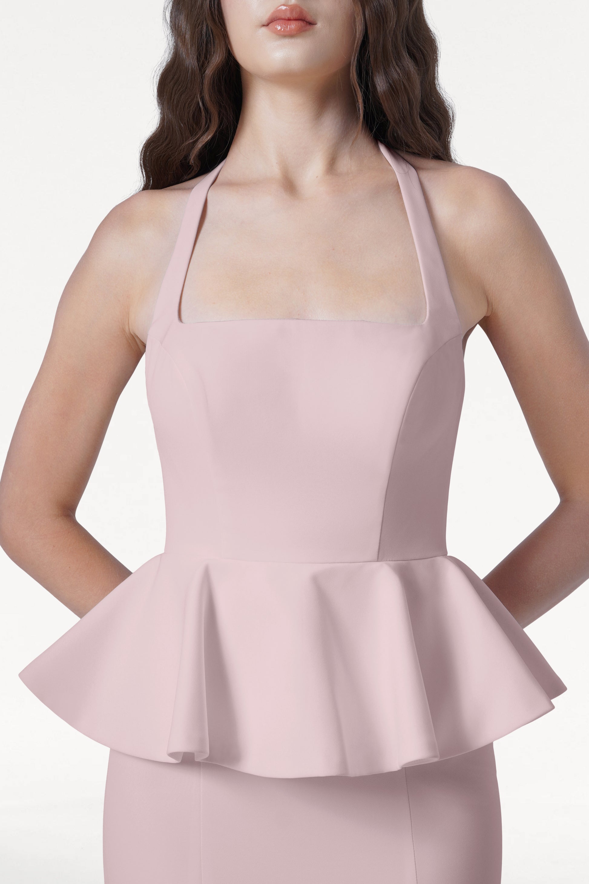 A woman wears the TH&TH Peony Bridesmaid Dress in Smoked Blush—a pale pink, sleeveless peplum top with a square neckline and halter straps—shown from the waist up against a plain white background.