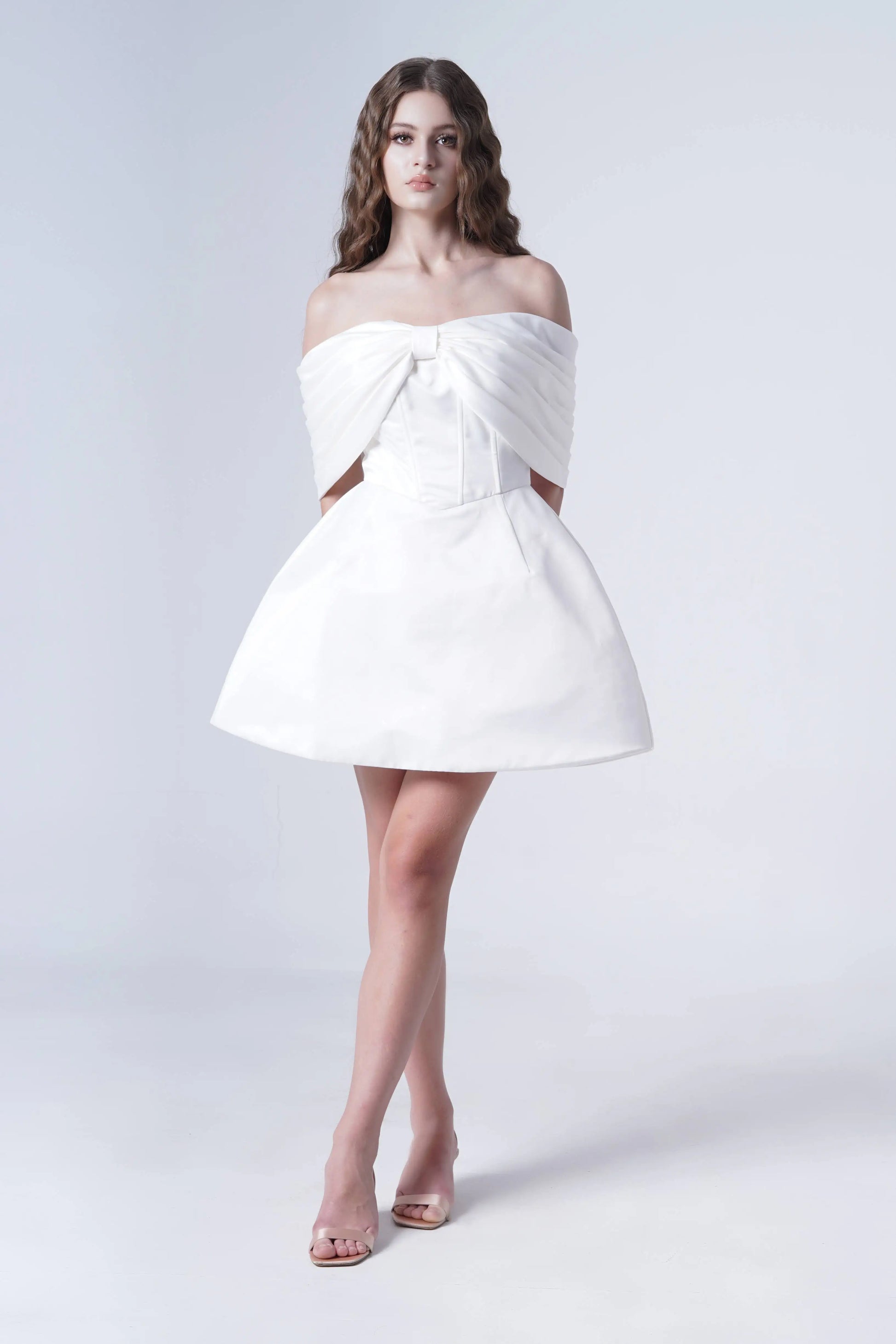 A woman wearing a strapless ivory dress with bow detail on a white background.