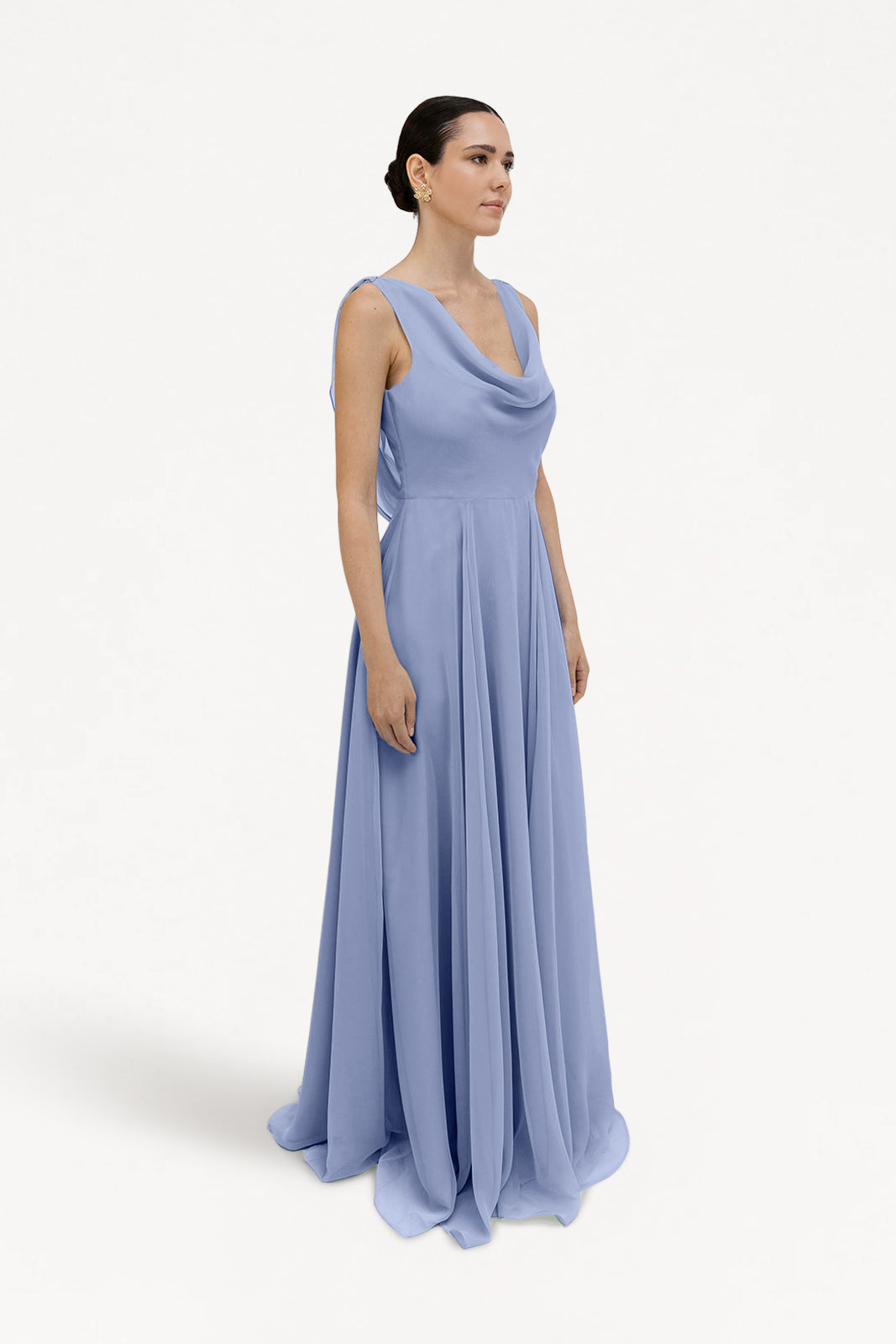 A woman with dark hair pulled back stands against a white background, wearing the TH&TH Athena Bridesmaid Dress in French Blue Chiffon—a sleeveless, floor-length dress featuring a draped neckline.
