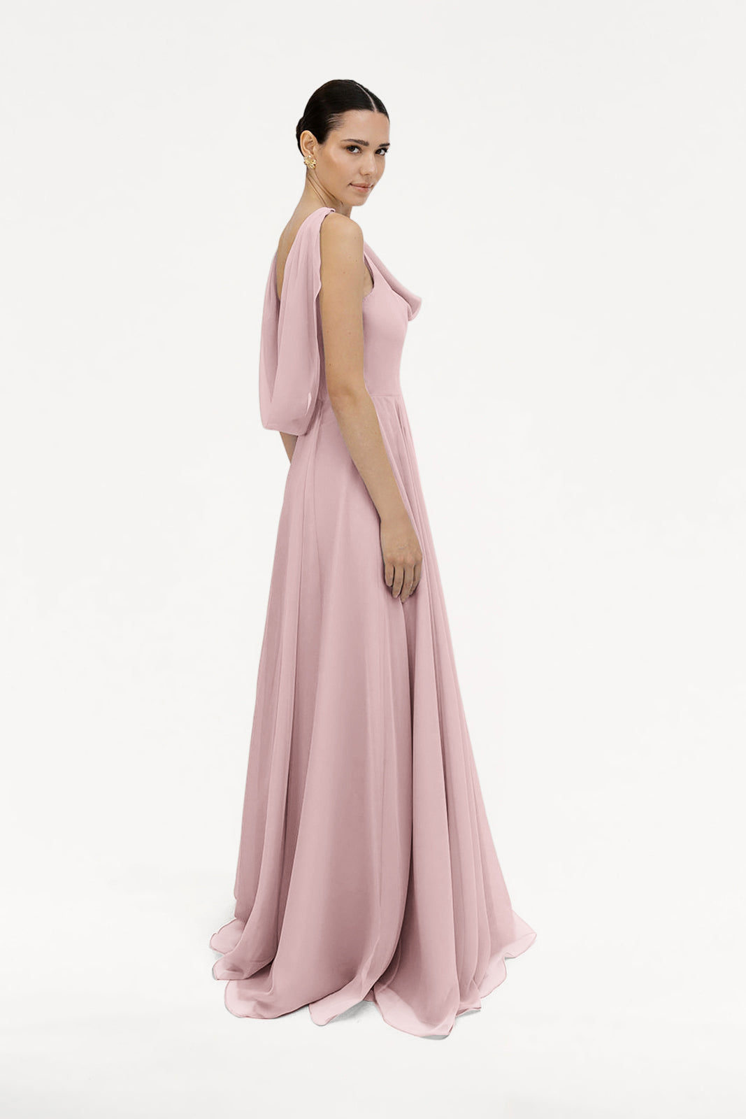 A woman poses in profile against a plain white background, wearing the TH&TH Athena Bridesmaid Dress in smoked blush chiffon—a floor-length gown with draped sleeves.