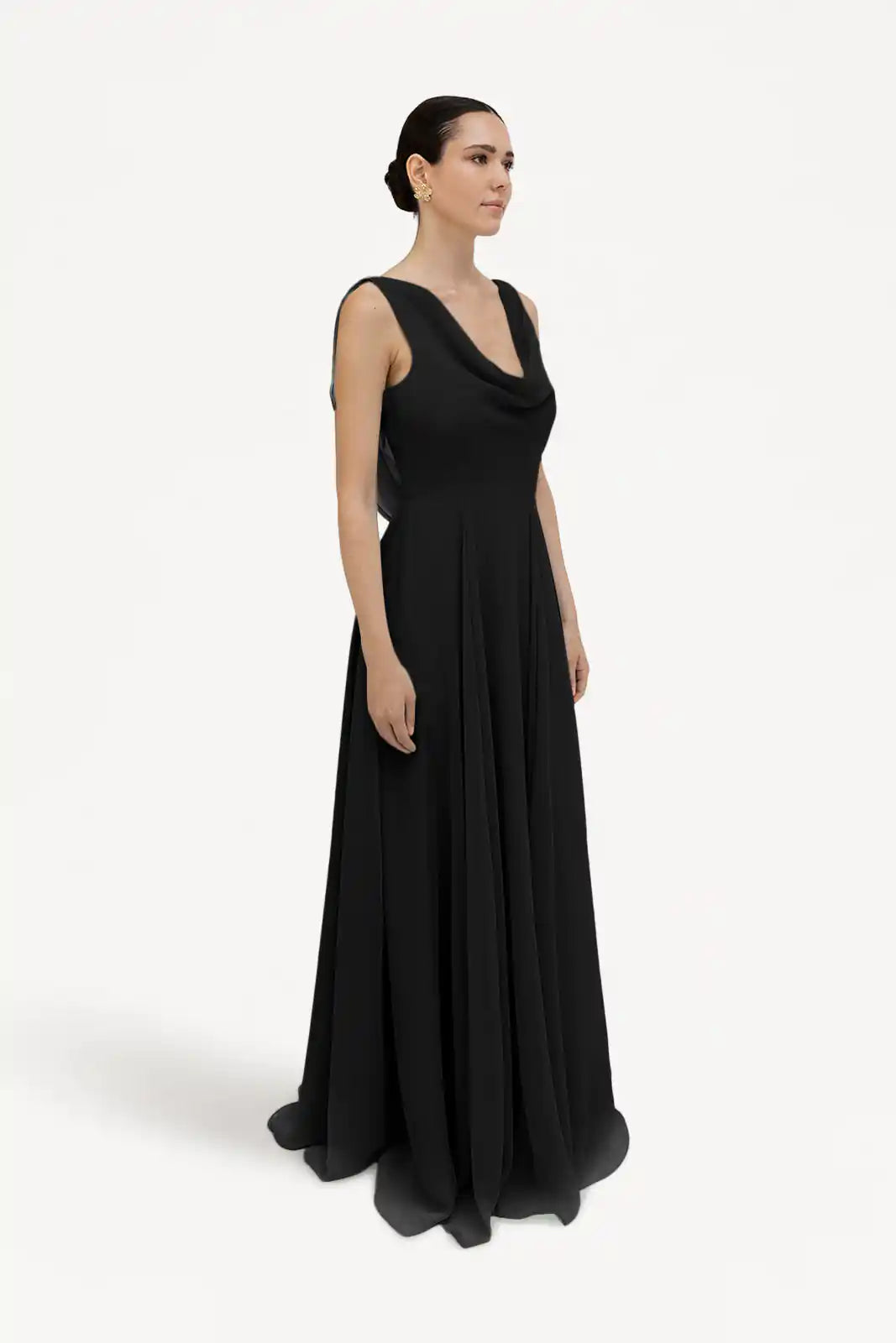 A woman models the TH&TH Athena Bridesmaid Dress in black chiffon, featuring a long, sleeveless design. She stands against a white background, hair pulled back, gazing calmly to the left.
