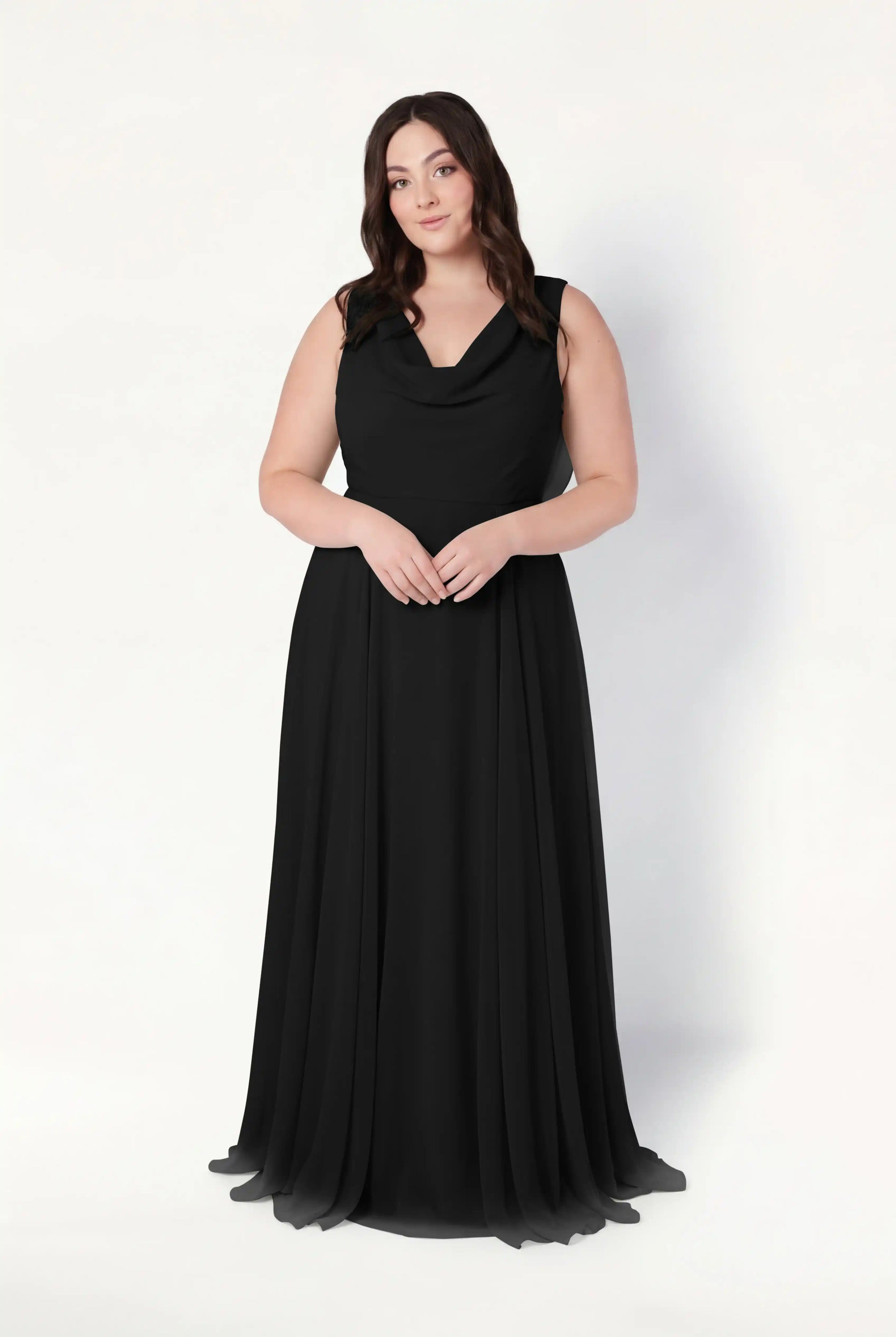 A woman with long brown hair stands against a white background, wearing the TH&TH Athena Bridesmaid Dress in Black Chiffon—a sleeveless, floor-length gown with a cowl neck and flowing fabric, perfect as a modern bridesmaid dress.