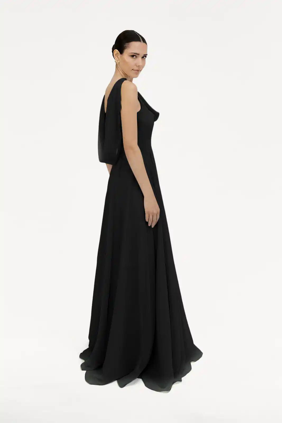 A woman models the TH&TH Athena Bridesmaid Dress in Black Chiffon, standing against a plain white background with her hair pulled back and glancing over her shoulder.