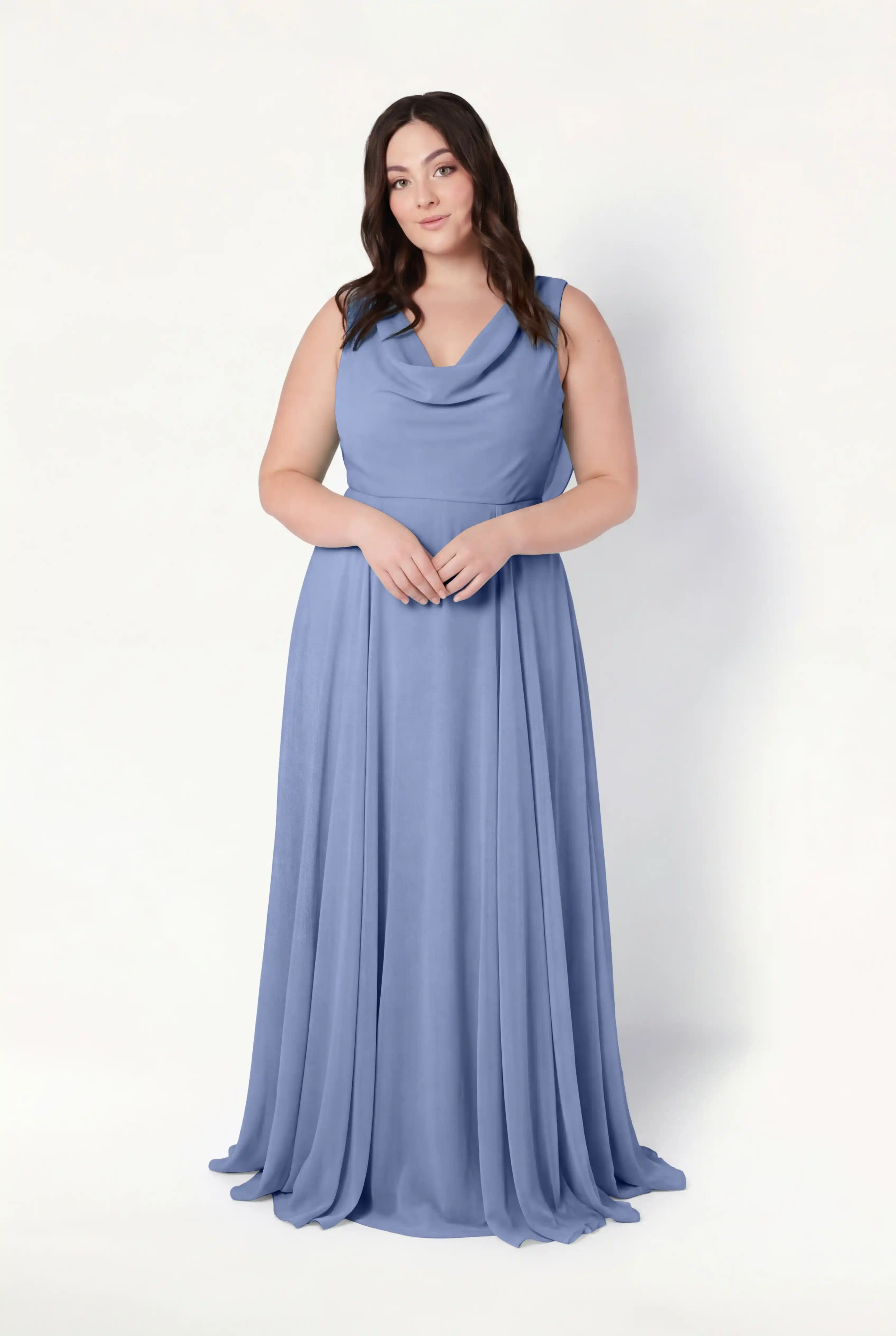 A woman with long brown hair wears the TH&TH Athena Bridesmaid Dress in French Blue Chiffon, featuring a sleeveless, floor-length design and cowl neck, standing against a plain white background with her hands clasped in front.