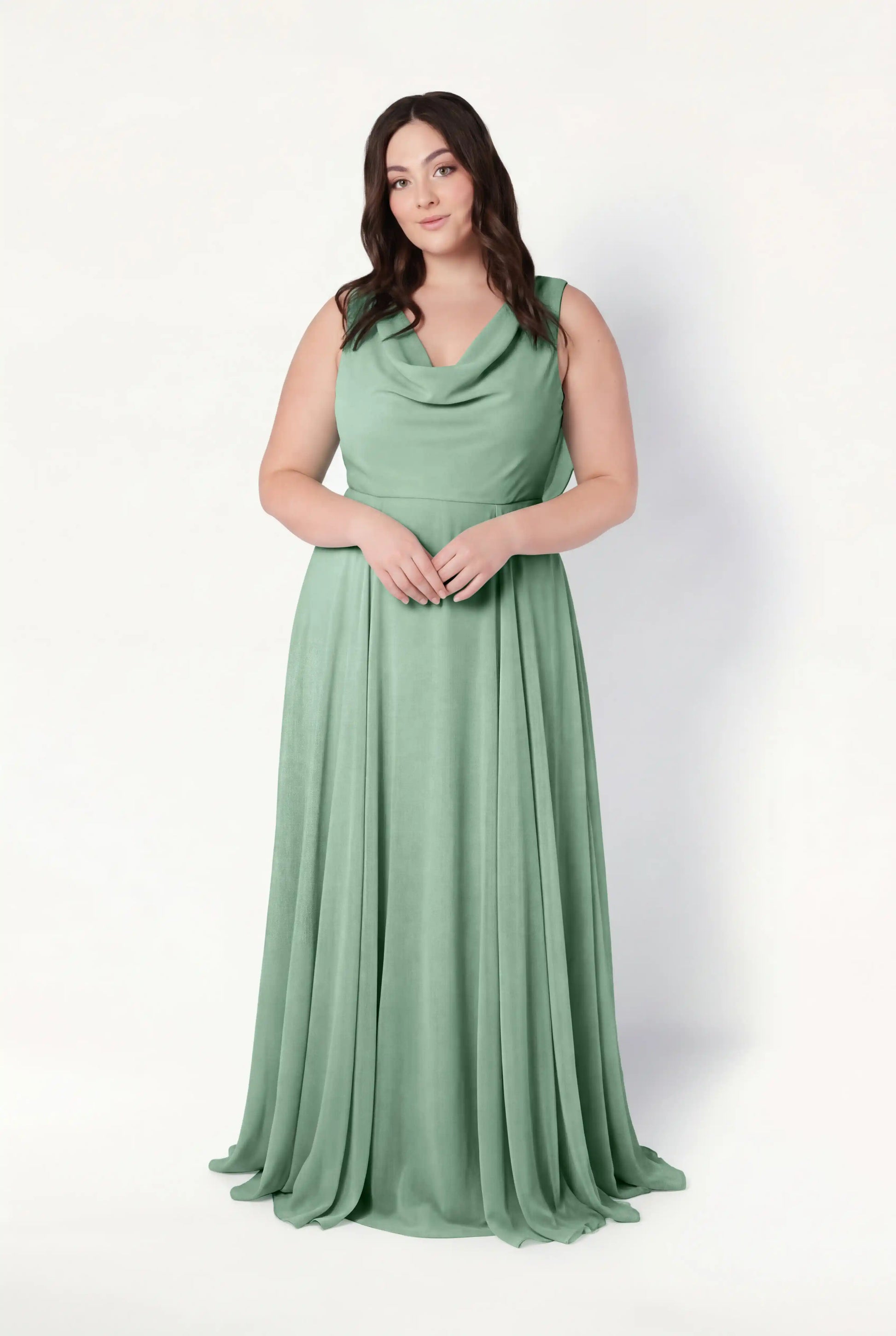 A woman with long brown hair models the TH&TH Athena Bridesmaid Dress in sage green chiffon, a sleeveless, floor-length gown with a draped cowl neck, standing against a plain white background.