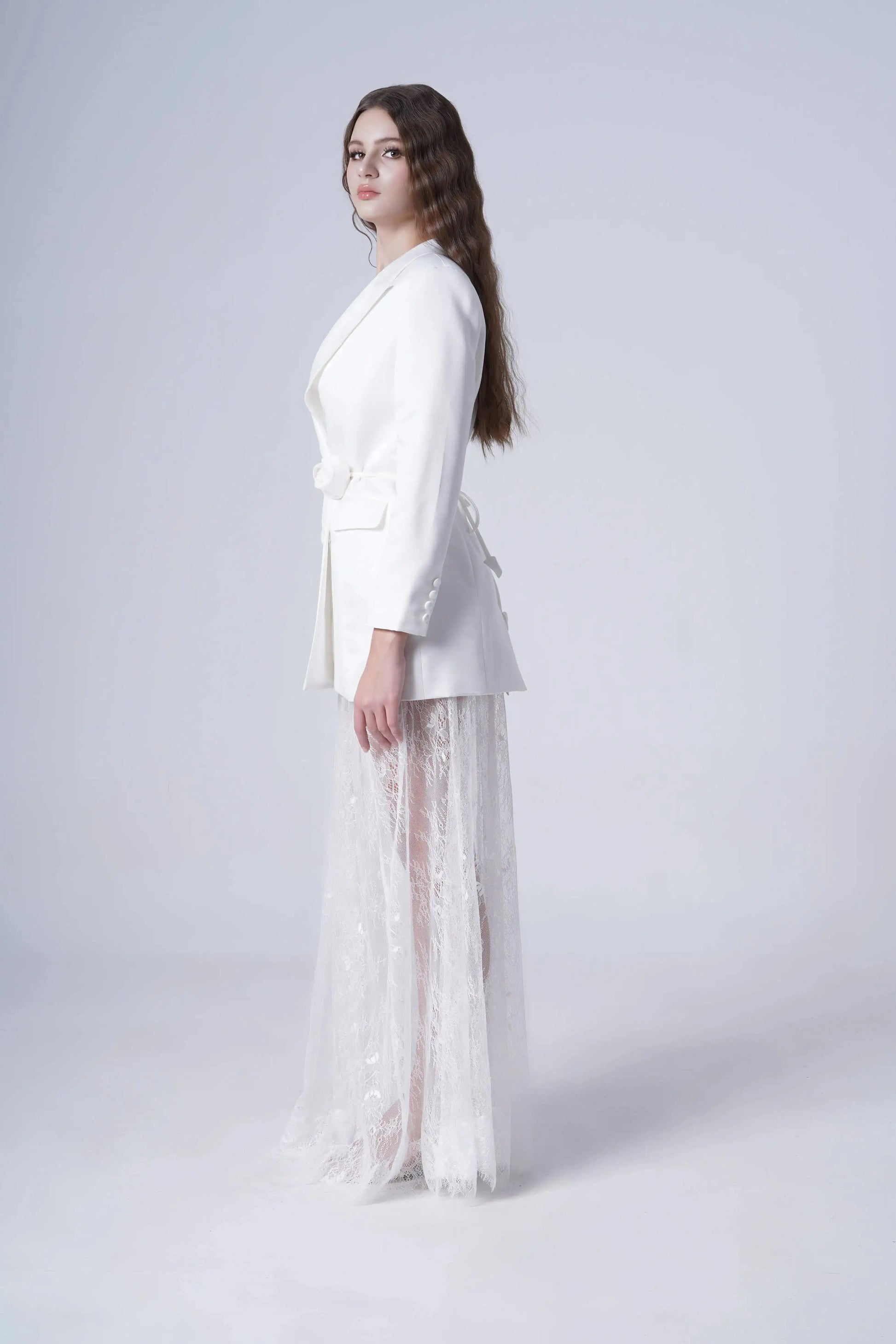 Woman wearing a white blazer with sheer lace skirt on a white background