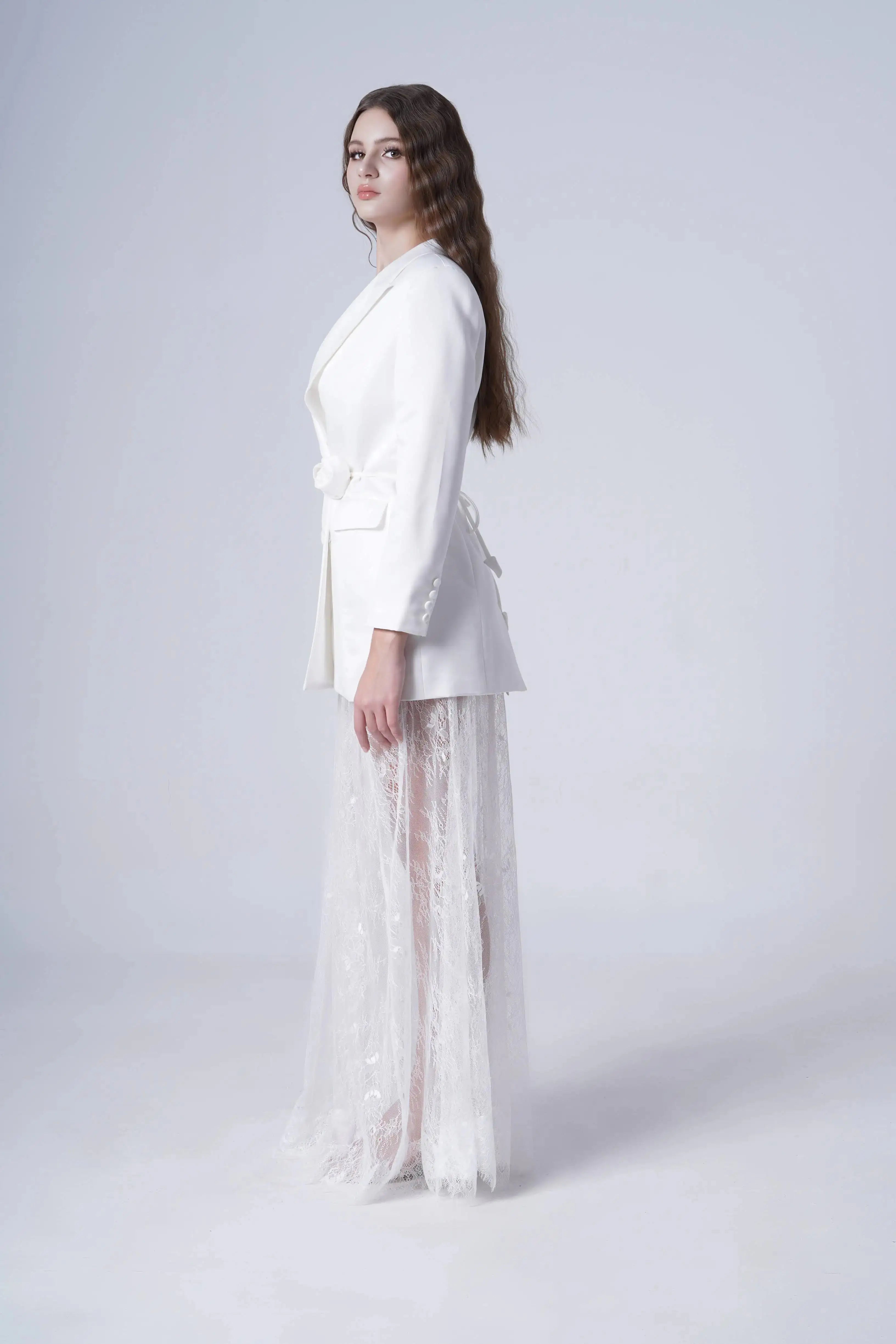 Woman wearing a white blazer with sheer lace skirt on a white background