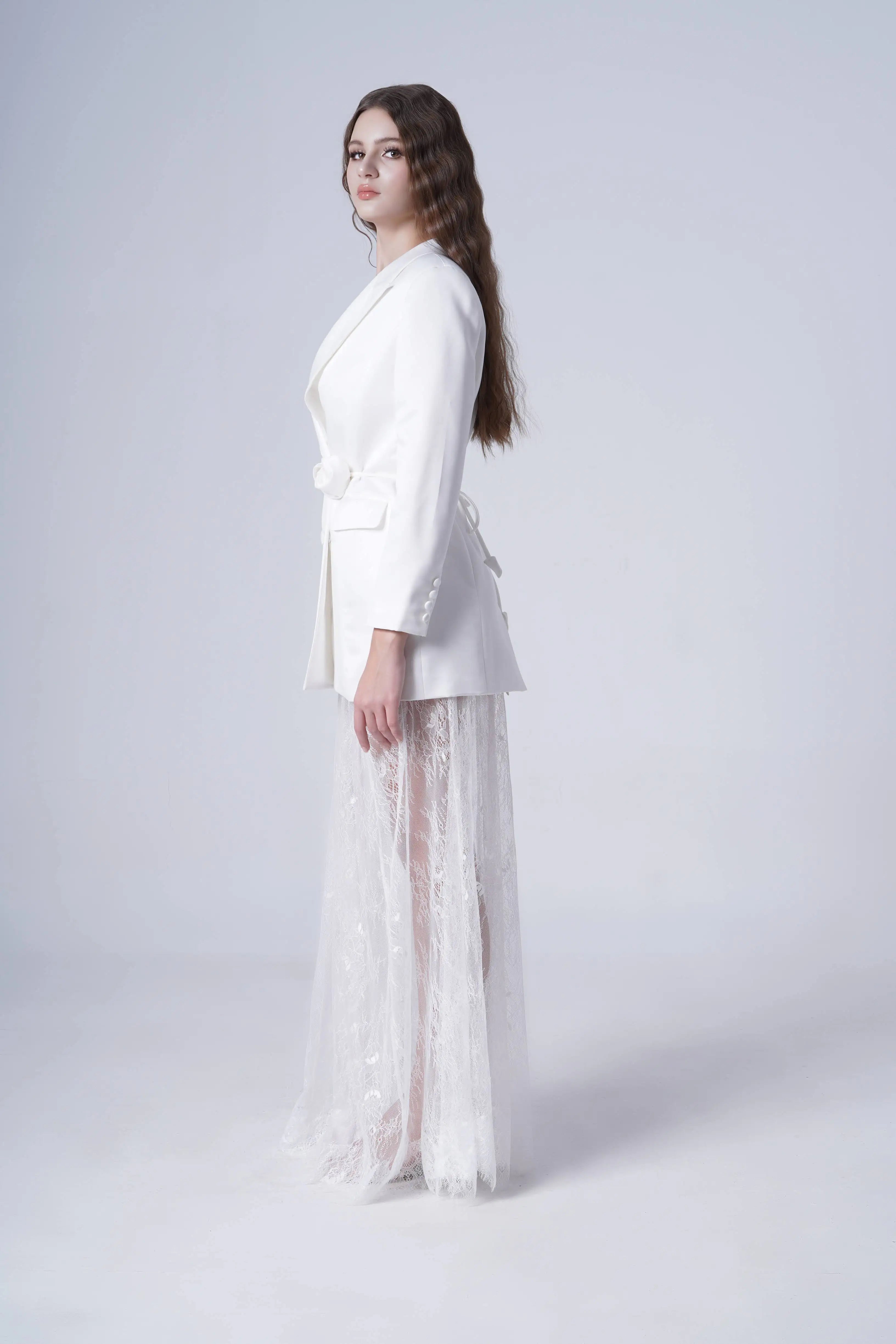Woman wearing a white blazer with sheer lace skirt on a white background