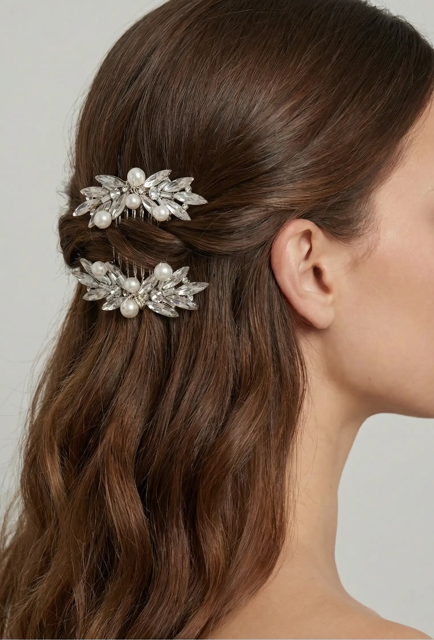 A woman with brown wavy hair styled half-up wears the TH&TH Beaumont Crystal and Pearl Leaf Hair Comb (2pcs), shown from the side against a plain background.