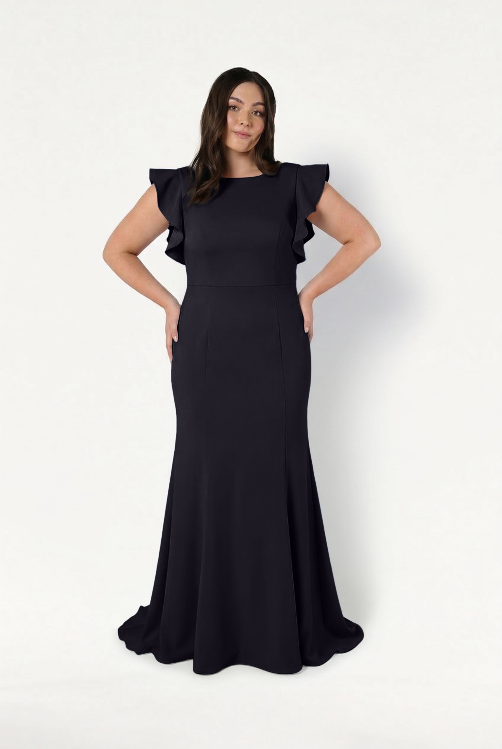 A woman models the TH&TH Cecelia Moss Crepe Bridesmaid Dress in Black—a floor-length, fitted gown with ruffled short sleeves—standing against a white background with hands on hips and a soft smile.