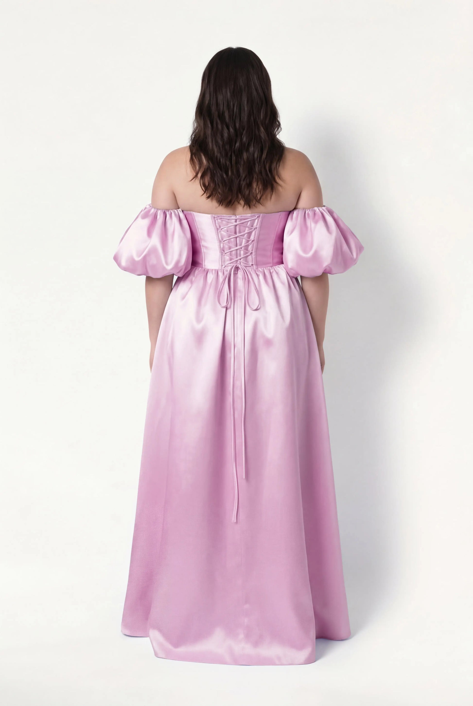 A woman with long brown hair models the TH&TH Blair Bridesmaid Dress in bubblegum pink satin twill, featuring an off-the-shoulder neckline, puffed short sleeves, a lace-up back, and a shiny finish against a plain white background.