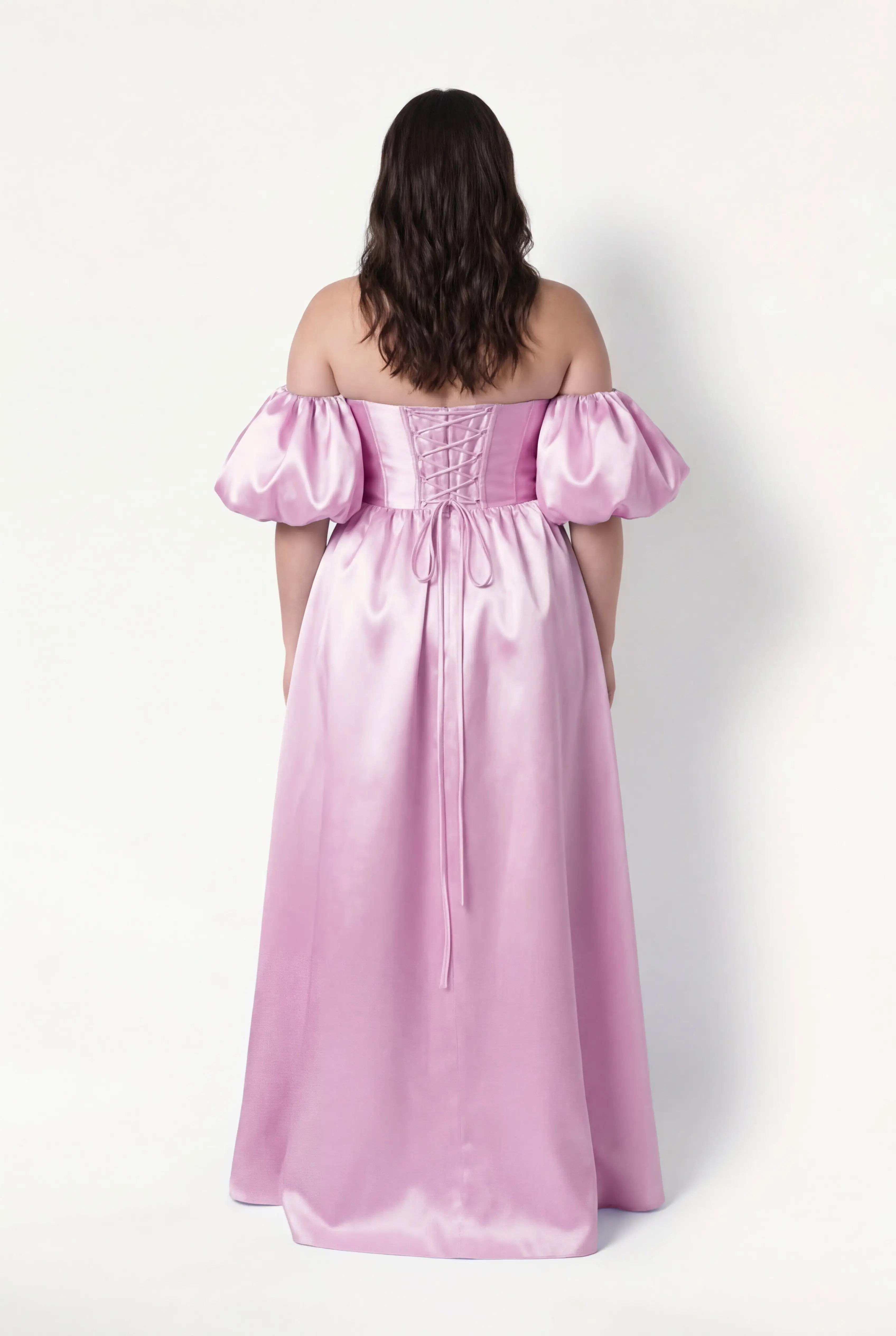 A woman with long brown hair models the TH&TH Blair Bridesmaid Dress in bubblegum pink satin twill, featuring an off-the-shoulder neckline, puffed short sleeves, a lace-up back, and a shiny finish against a plain white background.