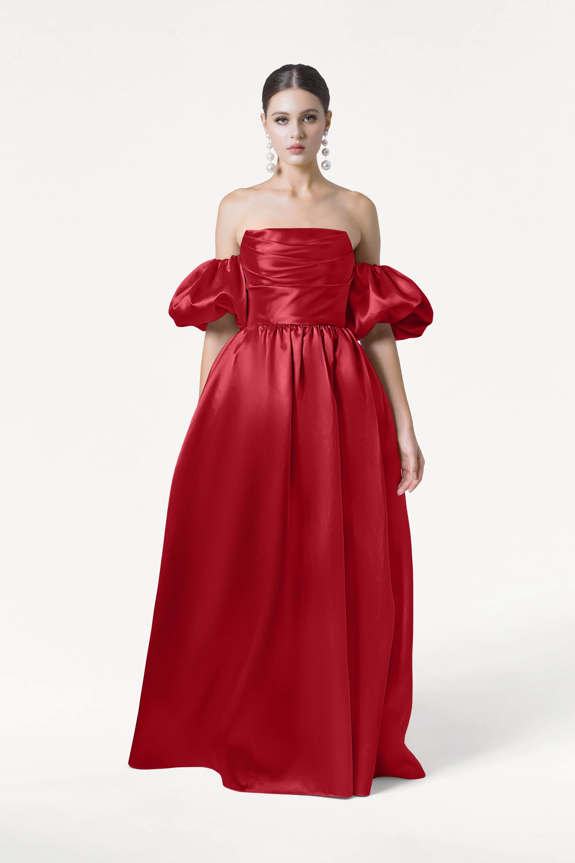 A woman models the Blair Bridesmaid Dress in Dark Cherry Satin Twill by TH&TH, featuring detachable puff sleeves and a fitted bodice, against a white background. Her dark hair is pulled back, and she wears large dangling earrings.
