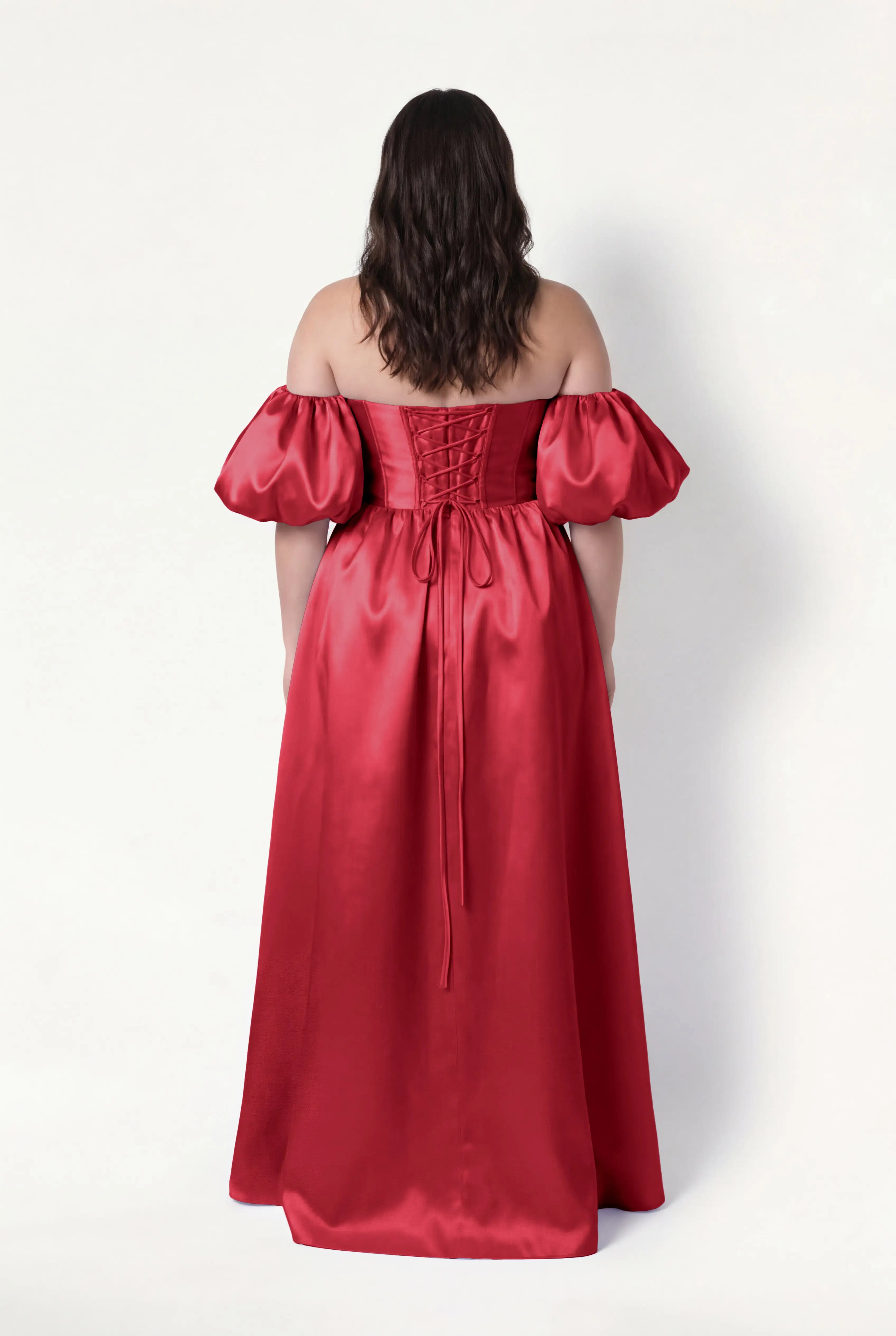 A woman with wavy brown hair faces away, modeling the TH&TH Blair Bridesmaid Dress in dark cherry satin twill, featuring detachable puff sleeves and a lace-up back, against a plain white background.