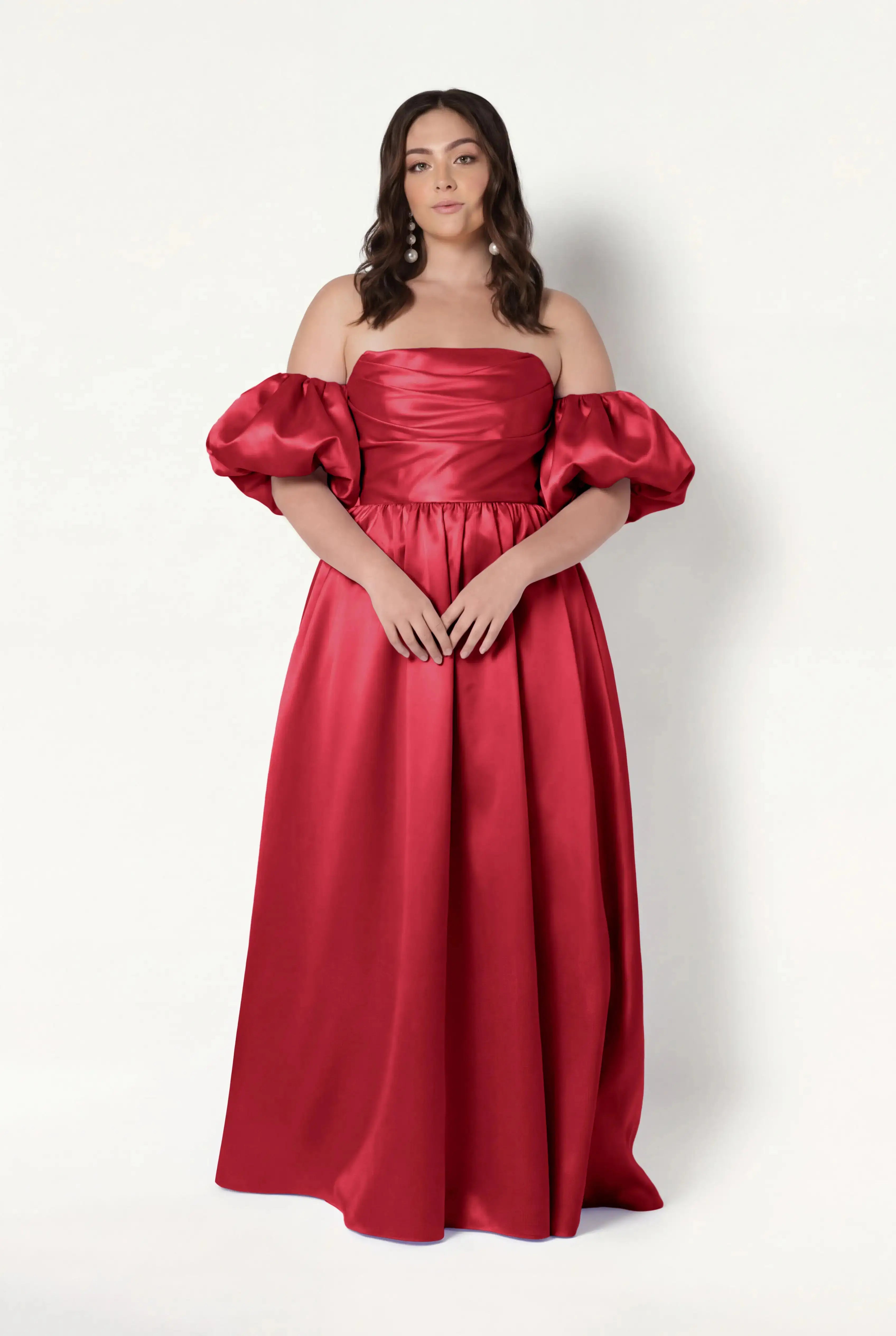 A woman wears the TH&TH Blair Bridesmaid Dress in Dark Cherry Satin Twill, a long off-the-shoulder gown with detachable puff sleeves, standing against a plain white background.
