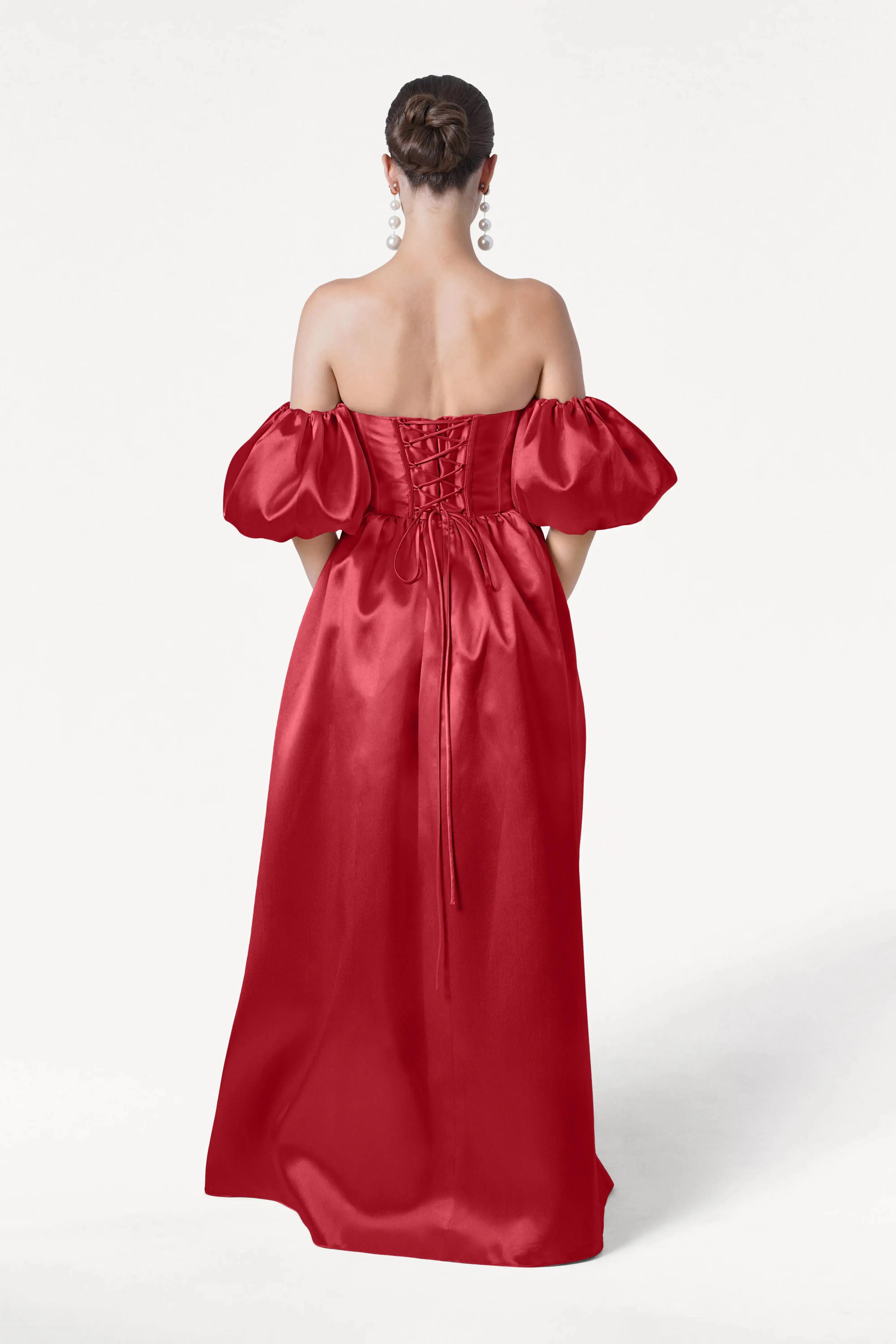 A woman with her hair in a bun is seen from the back wearing the Blair Bridesmaid Dress in Dark Cherry Satin Twill by TH&TH, featuring detachable puff sleeves, a lace-up bodice, and large earrings for an elegant, romantic look.