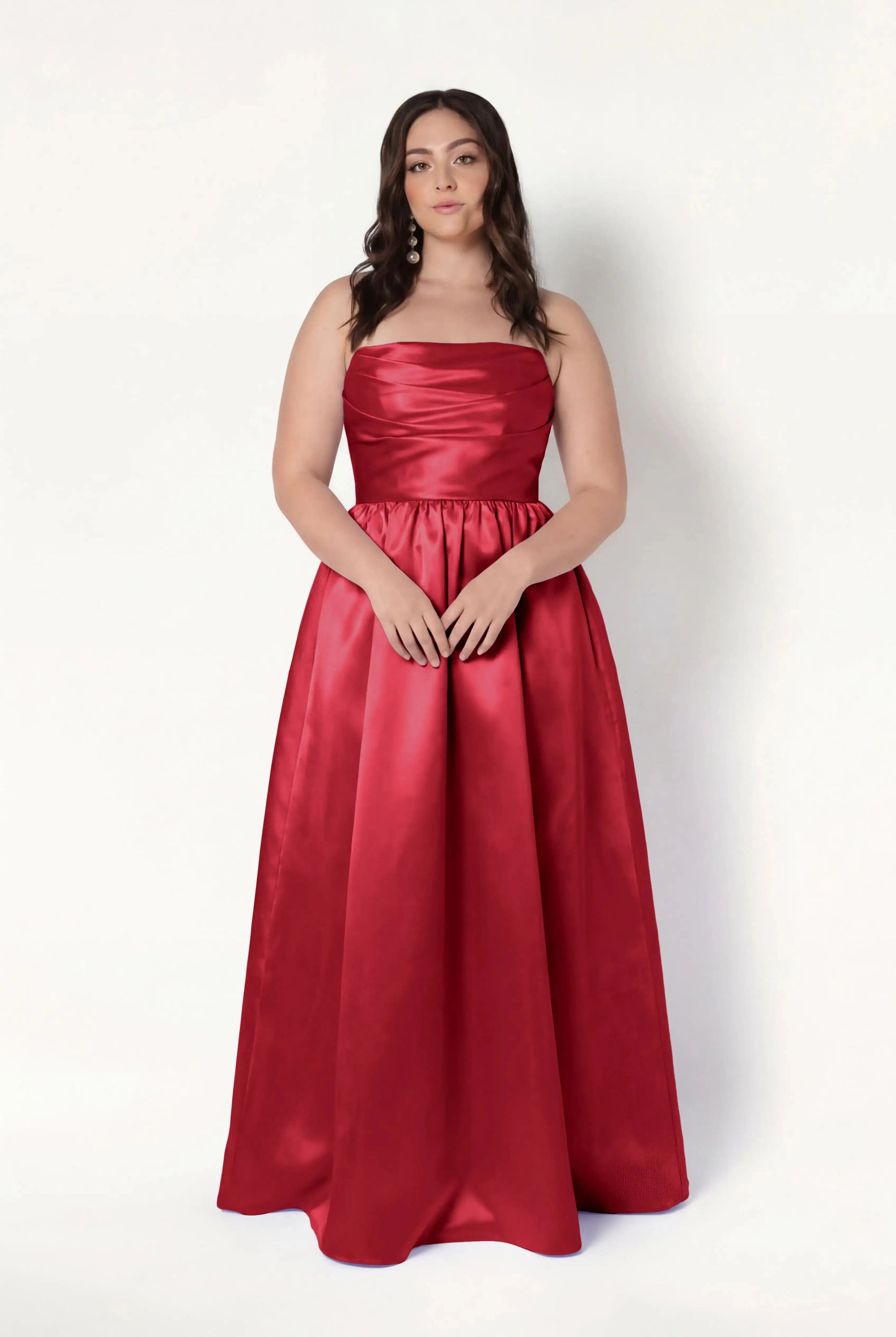 A woman with long, wavy brown hair wears the Blair Bridesmaid Dress in Dark Cherry Satin Twill by TH&TH. She stands against a plain white background, facing forward with her hands resting on her skirt.