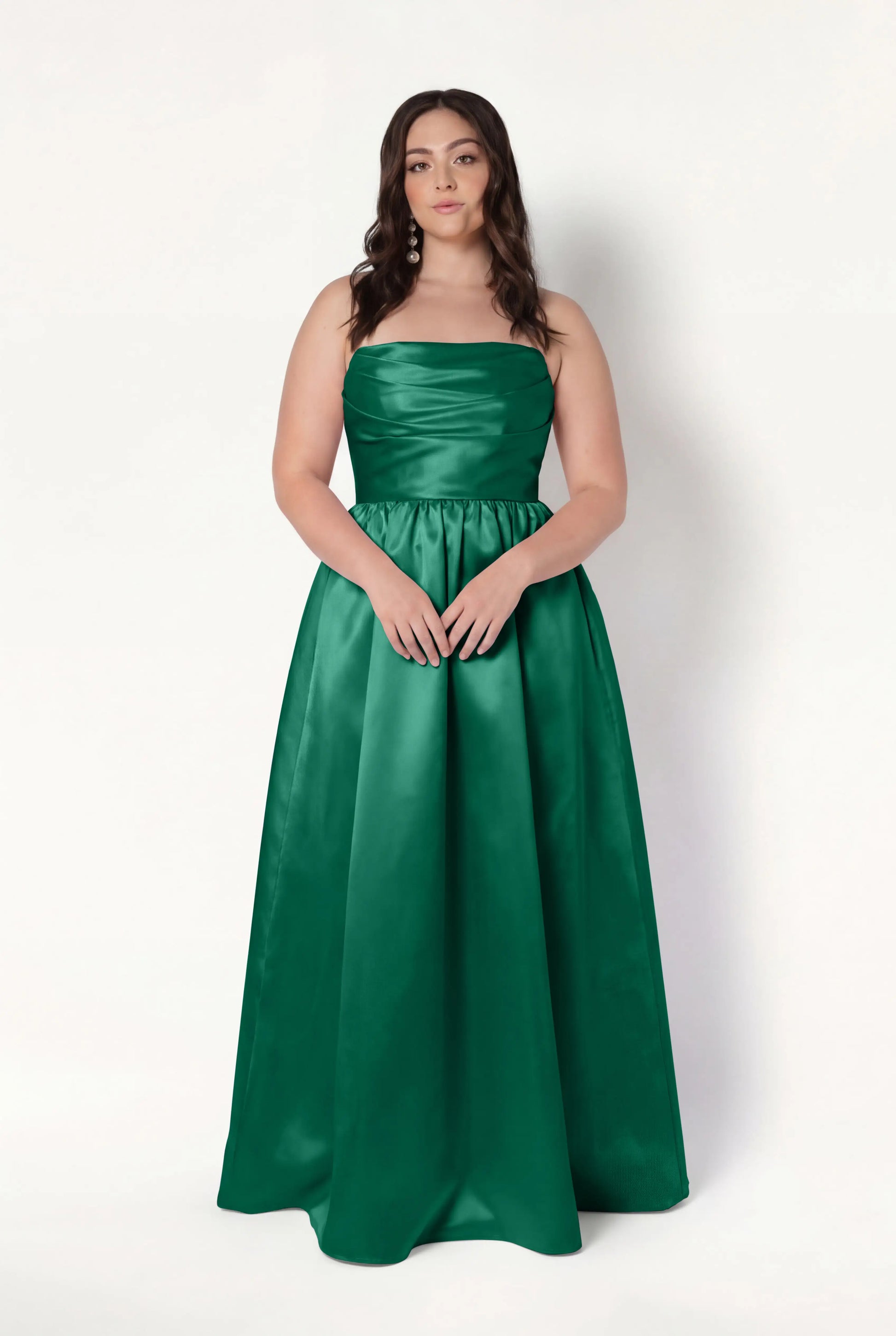 A woman with long brown hair wears the TH&TH Blair Bridesmaid Dress in Forest Green Satin Twill, standing against a plain white background.