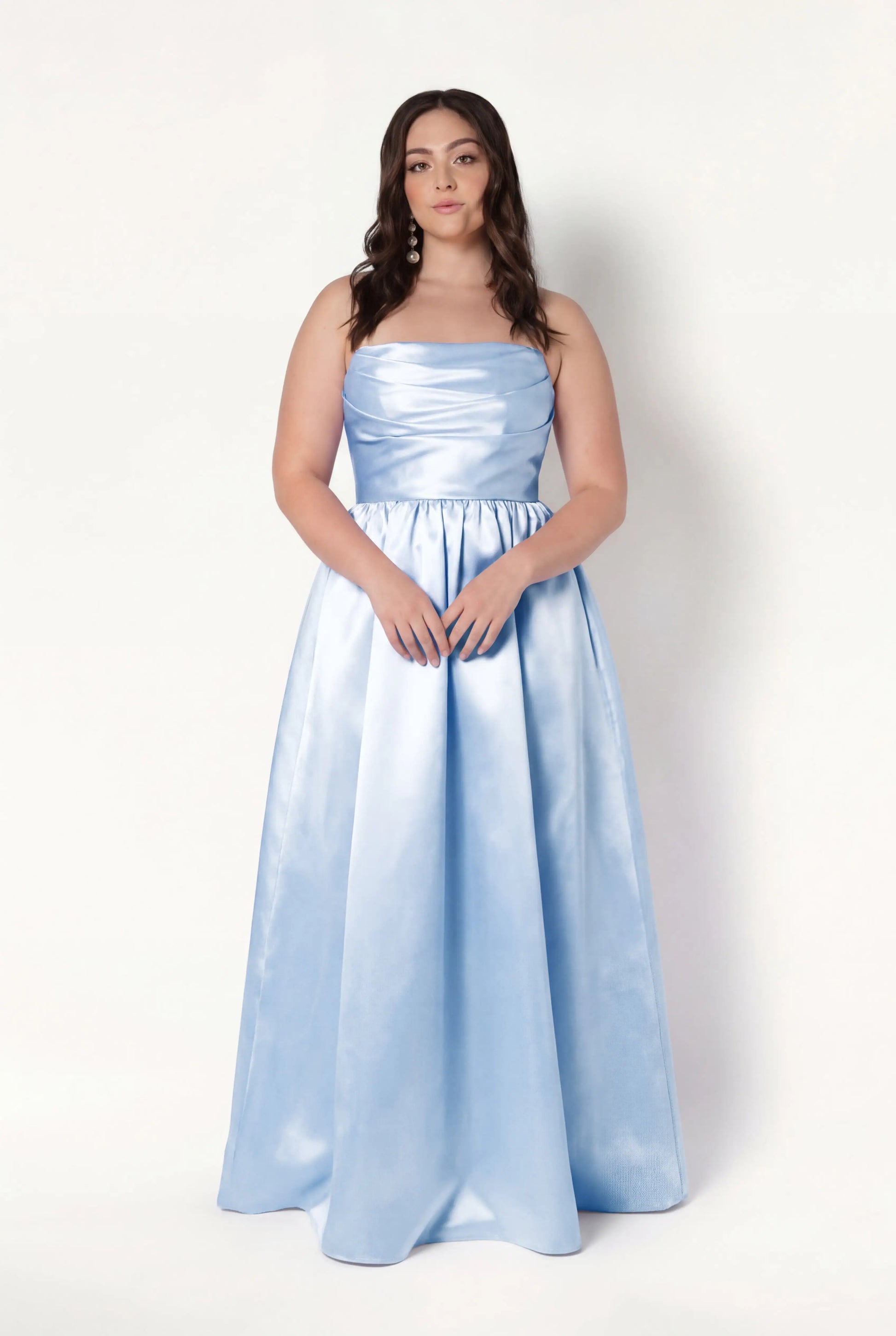 A woman with long brown hair wears the TH&TH Blair Bridesmaid Dress in Frosted Blue Satin Twill—strapless, floor-length, with detachable puff sleeves—standing against a plain white background and facing the camera neutrally.