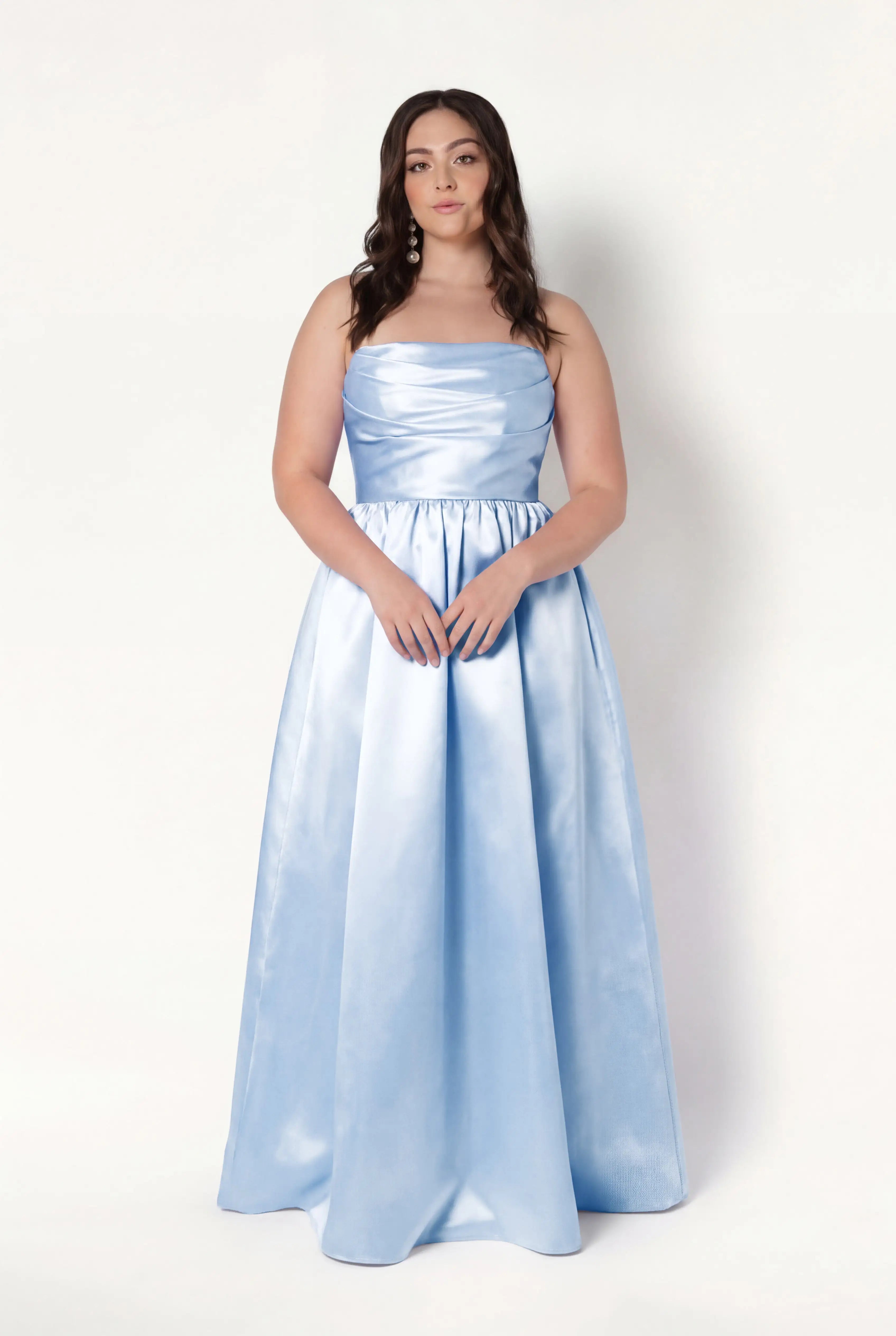 A woman with long brown hair wears the TH&TH Blair Bridesmaid Dress in Frosted Blue Satin Twill—strapless, floor-length, with detachable puff sleeves—standing against a plain white background and facing the camera neutrally.