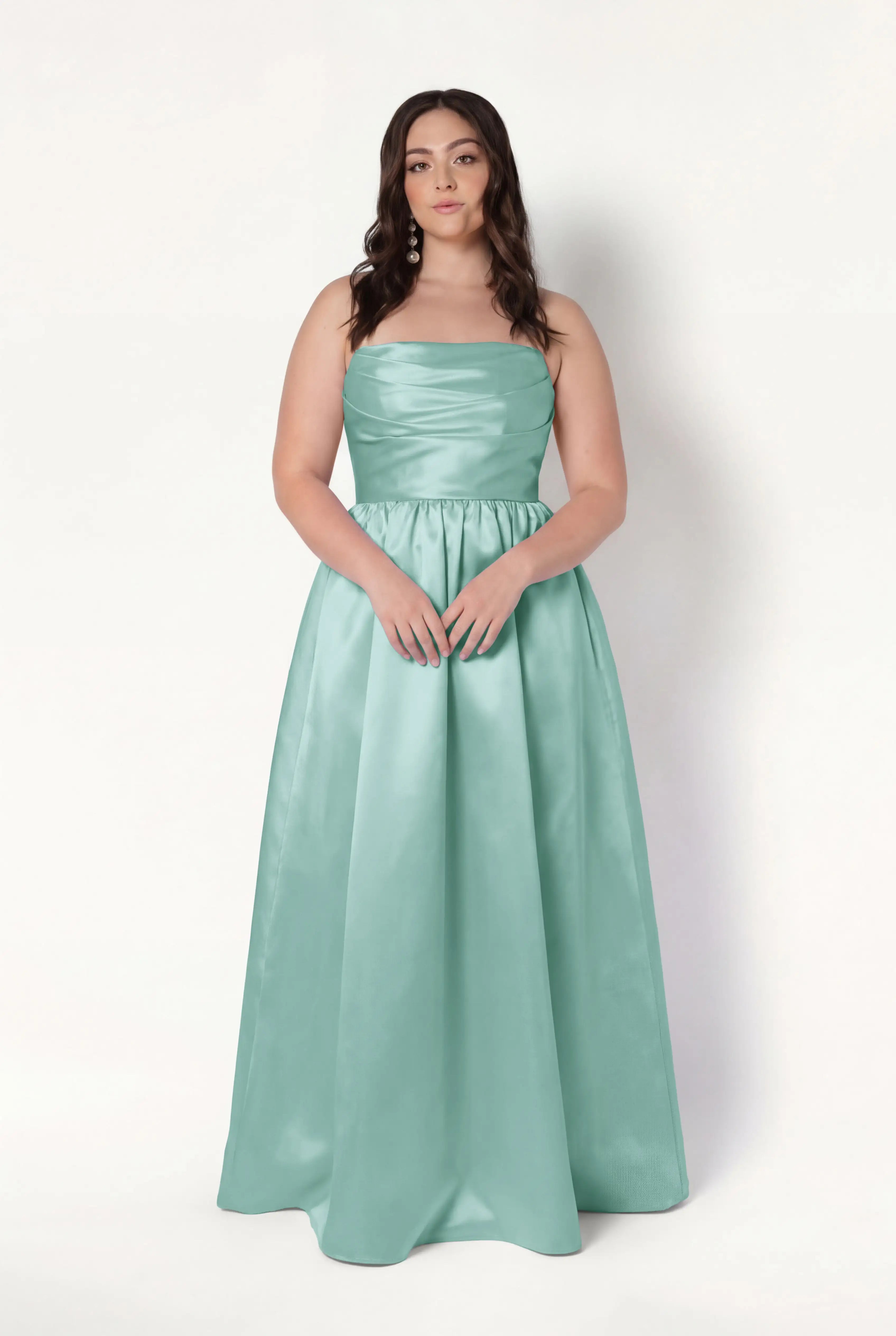 A woman with long dark hair models the TH&TH Blair Bridesmaid Dress in Seafoam Satin Twill. She stands against a plain white background, looking at the camera with her hands on her waist.