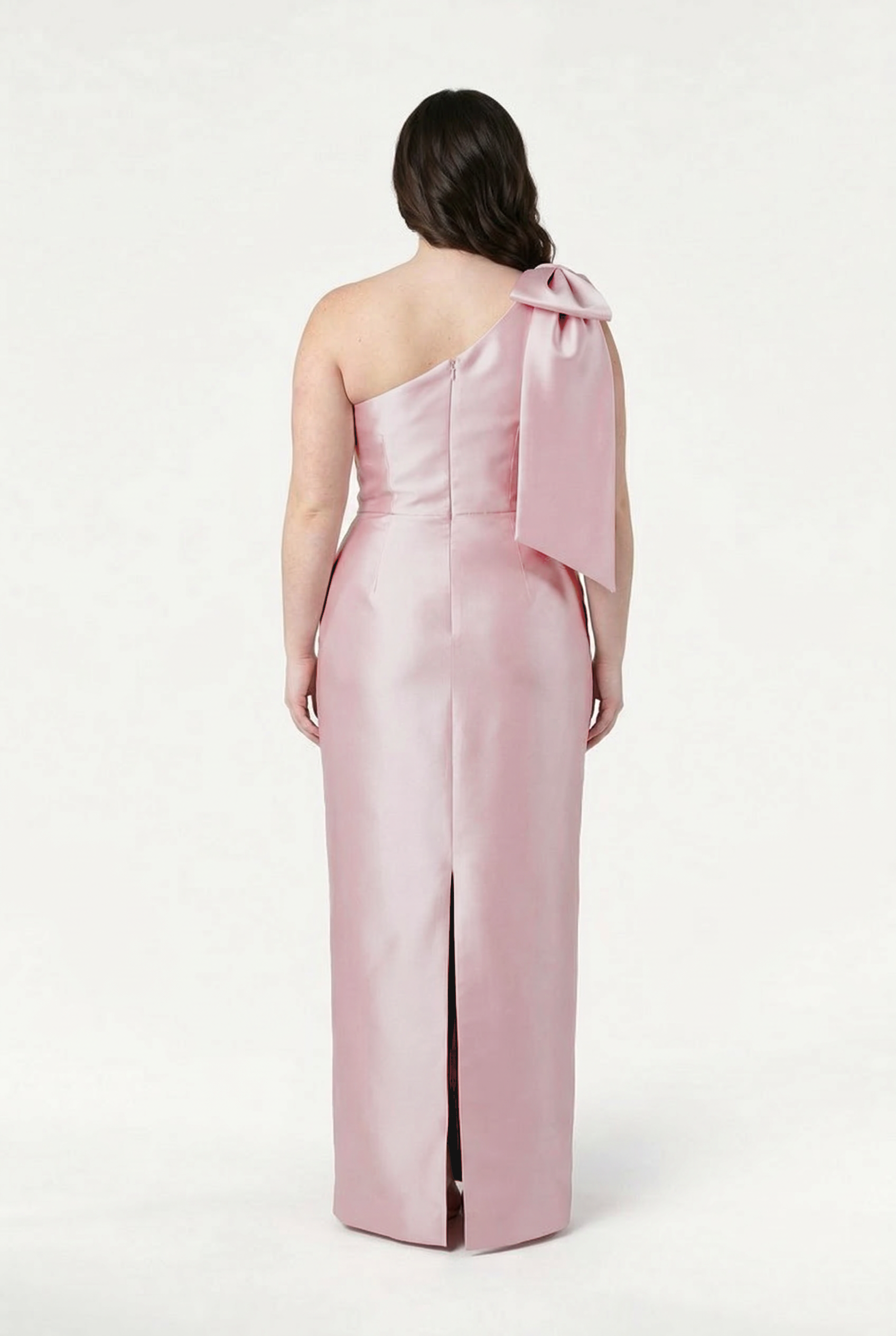 A woman wearing the TH&TH Ritz Bridesmaid Dress in Blush Pink Satin Twill stands facing away, highlighting the elegant back and statement shoulder bow, set against a plain white background.