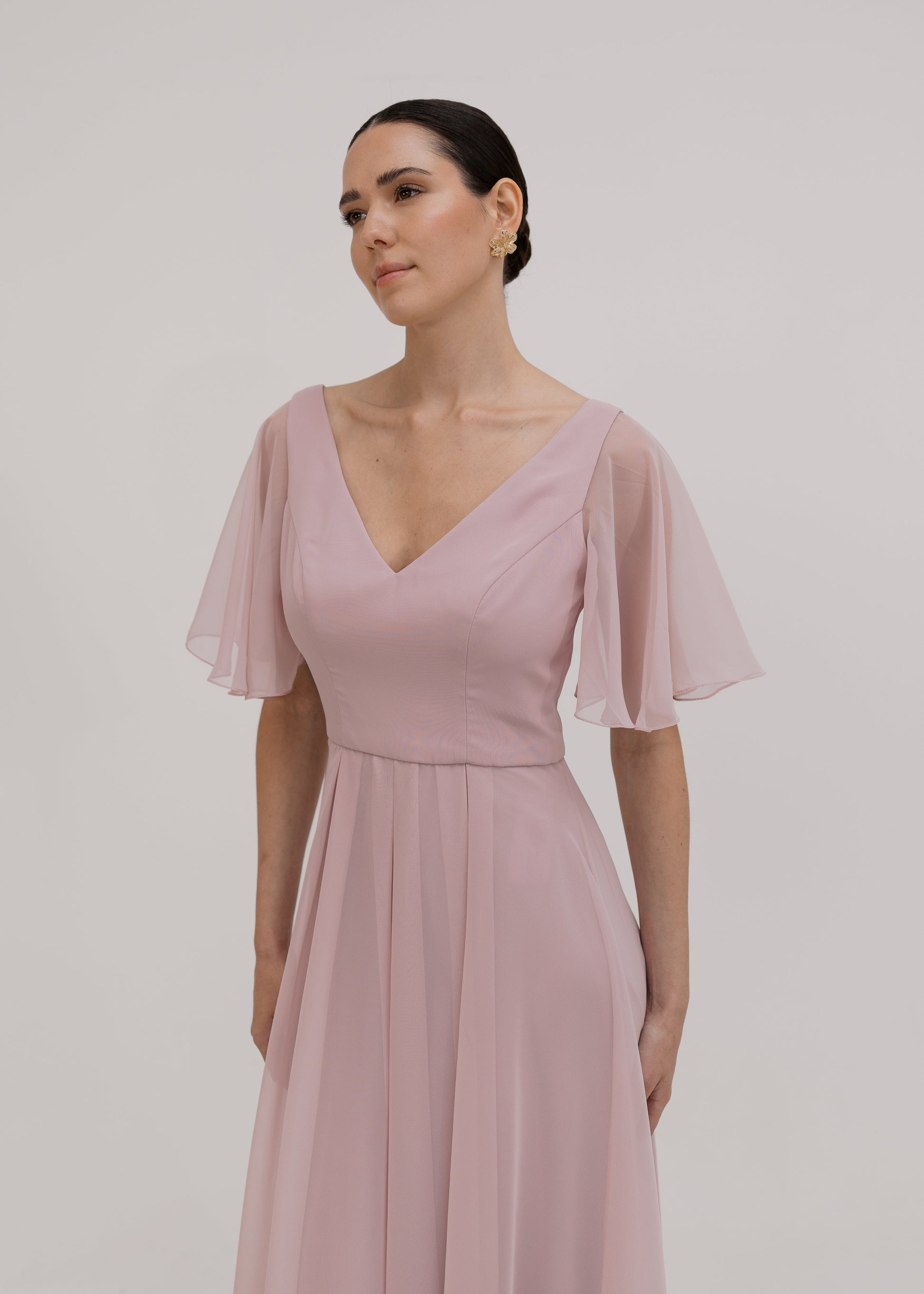Woman wearing a long smoked blush pink bridesmaid dress with V neck and full skirt in chiffon.