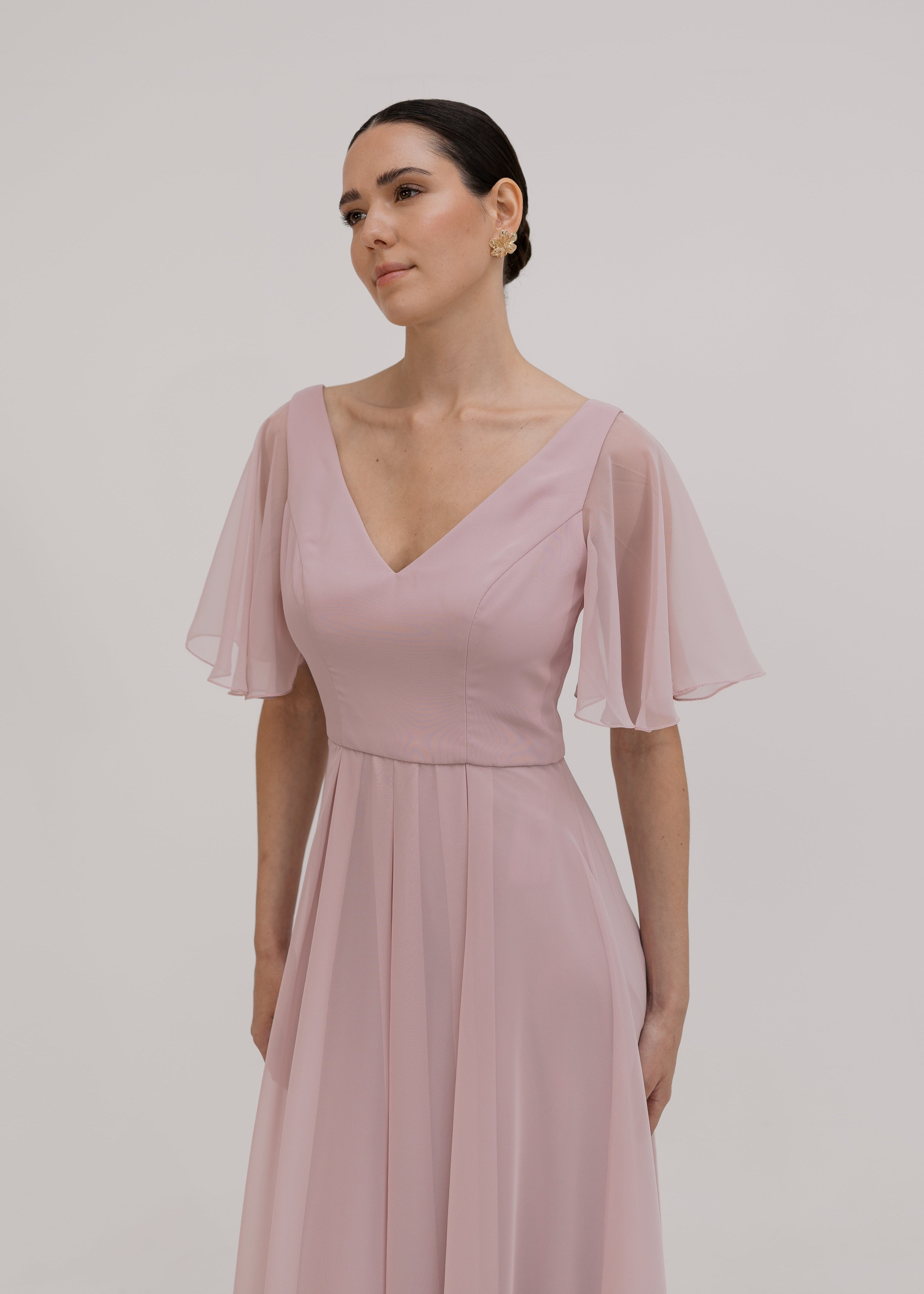 Woman wearing a long smoked blush pink bridesmaid dress with V neck and full skirt in chiffon.