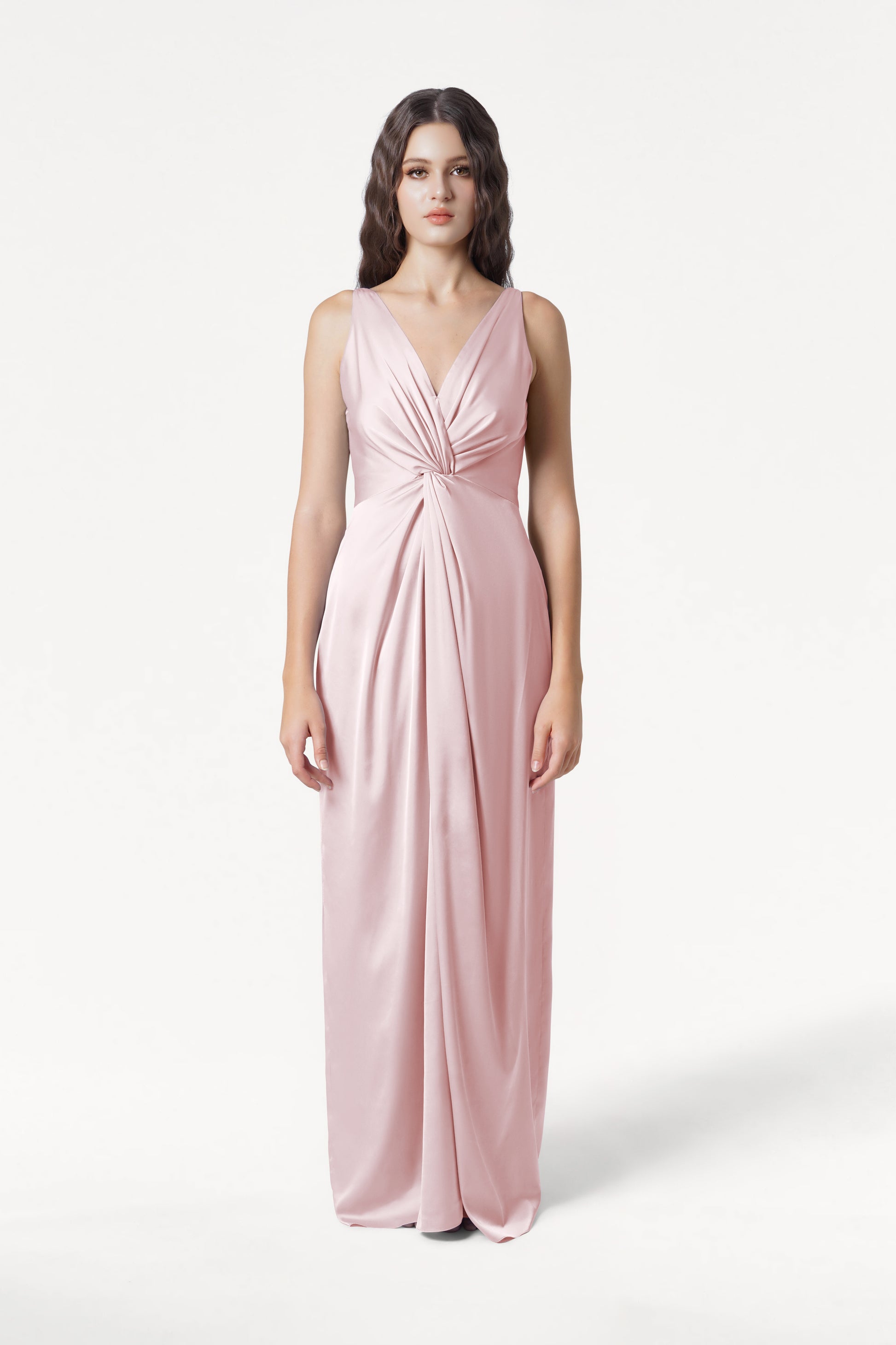 A woman models the TH&TH Carmen Bridesmaid Dress in blush pink satin, featuring a sleeveless, floor-length design with a twisted knot waist—an elegant pick for contemporary bridal parties.
