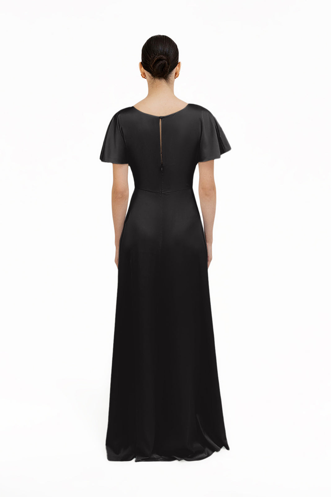 A woman with dark hair in a low bun stands with her back to the camera, modeling the TH&TH Camilla Bridesmaid Dress in Black Satin, a size-inclusive, short-sleeved gown, against a plain white background.