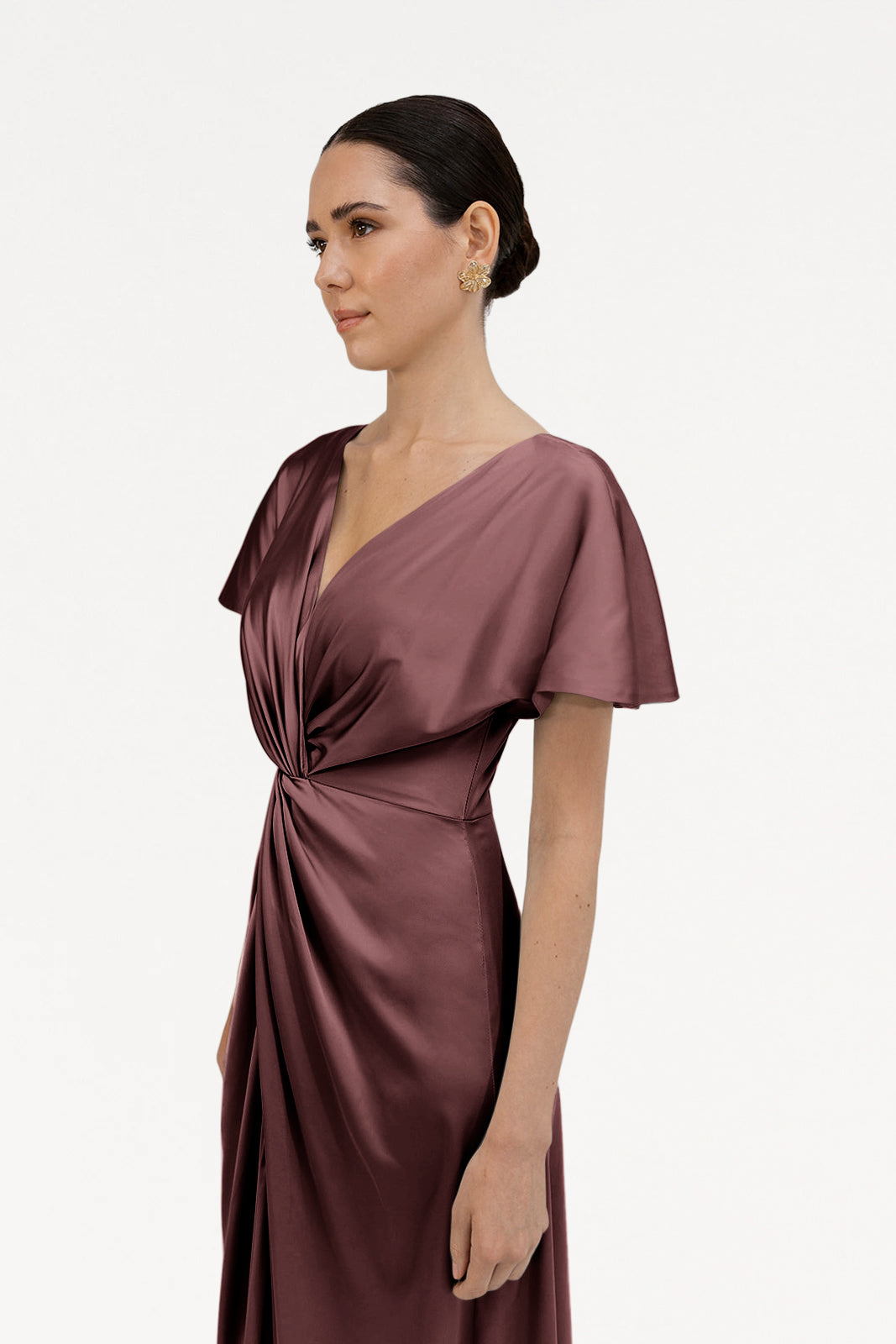 A woman with dark hair in a low bun wears the TH&TH Camilla Bridesmaid Dress in chocolate brown satin, featuring a deep V-neckline, flutter sleeves, and a gathered knot waist, standing against a plain white background.