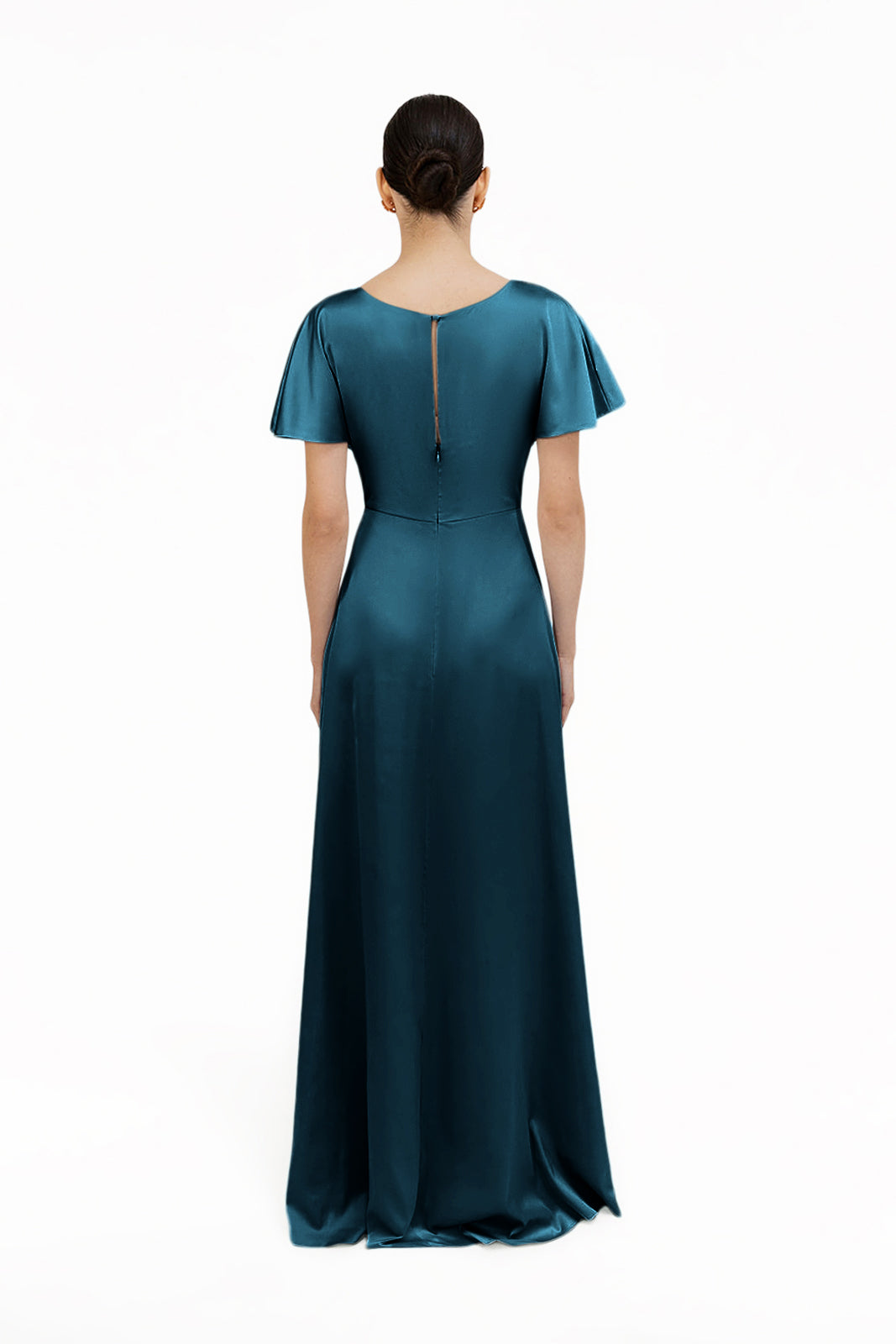 A woman with dark hair in a low bun models the TH&TH Camilla Bridesmaid Dress in Emerald Dawn Satin, featuring flutter sleeves and a back keyhole, standing against a plain white background. An elegant, modern gown shown from behind.
