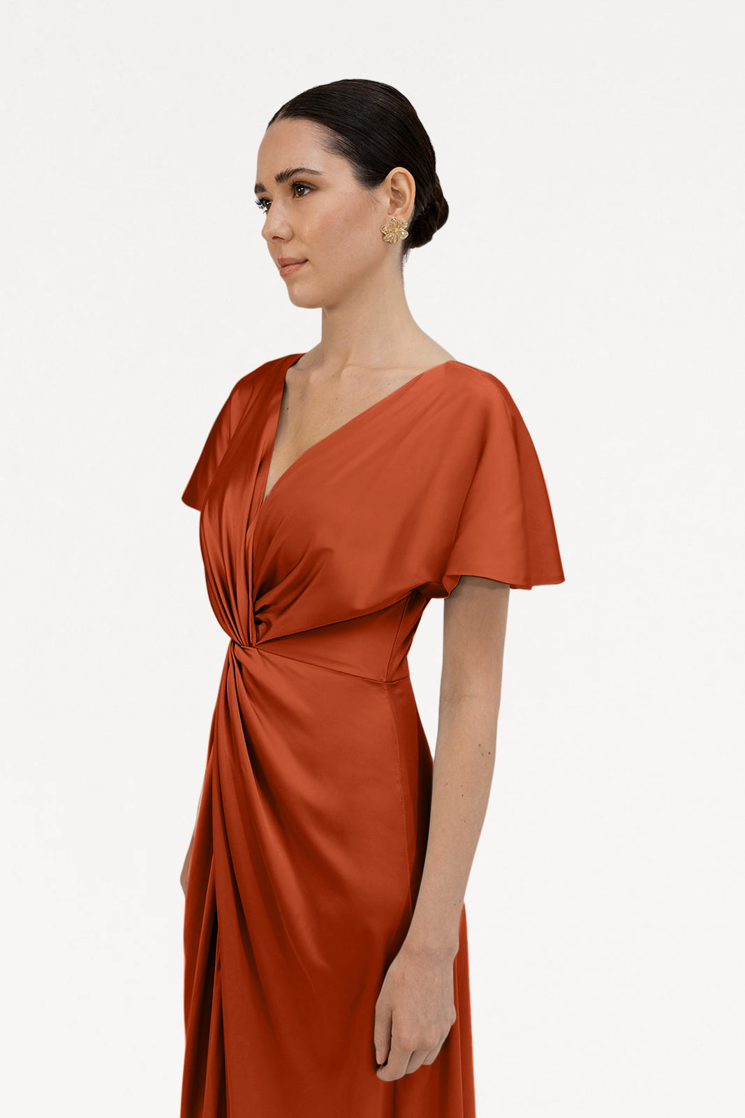 A woman with dark hair in an elegant updo models the TH&TH Camilla Bridesmaid Dress in Terracotta Satin, featuring short flutter sleeves and a twisted knot waist detail, standing against a plain white background.