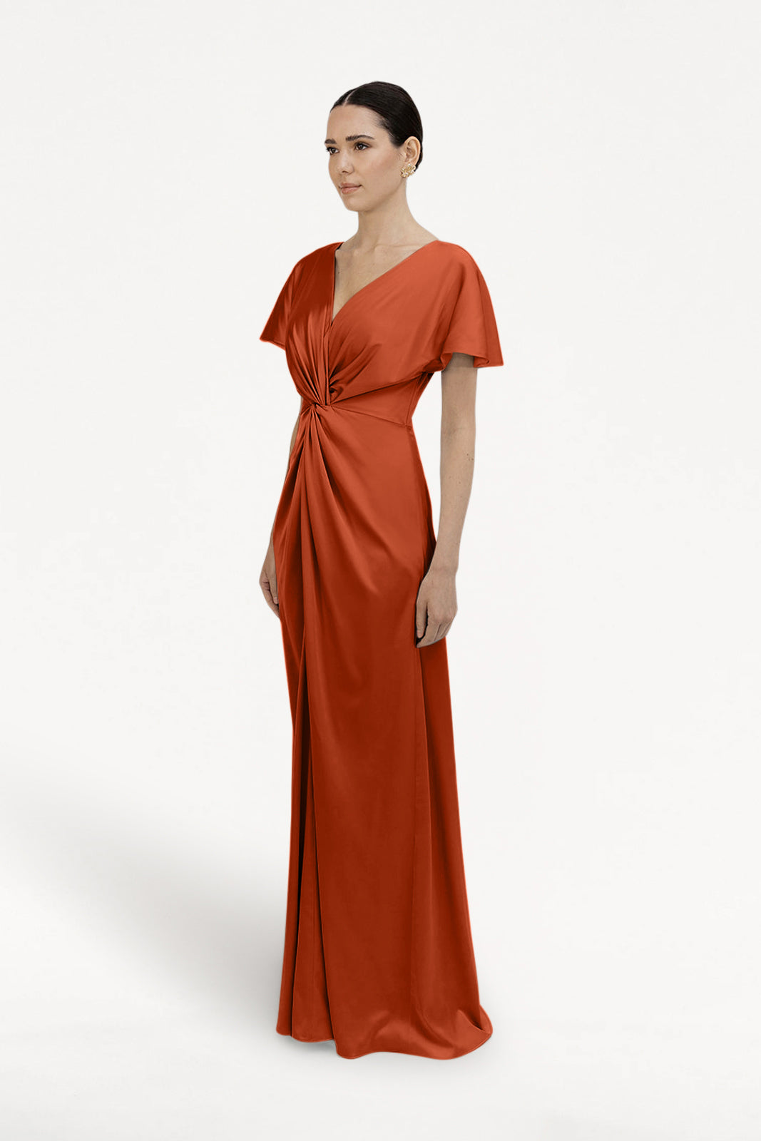 A woman models the TH&TH Camilla Bridesmaid Dress in terracotta satin, featuring short sleeves and a twisted knot waist detail, standing against a plain white background.