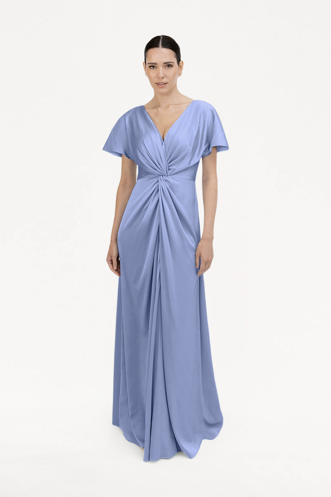 A woman poses against a white backdrop in the Camilla Bridesmaid Dress in French Blue Satin by TH&TH, a size-inclusive, floor-length gown with short sleeves, a twist-knot front bodice, and a flattering V-neckline.