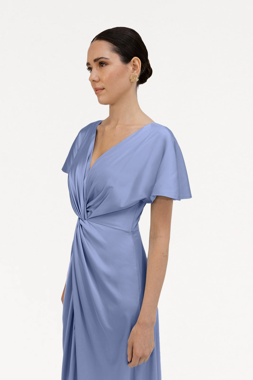 A woman with dark hair in an updo models the TH&TH Camilla Bridesmaid Dress in French Blue Satin, featuring short sleeves and a twist-knot bodice, standing against a plain white background.