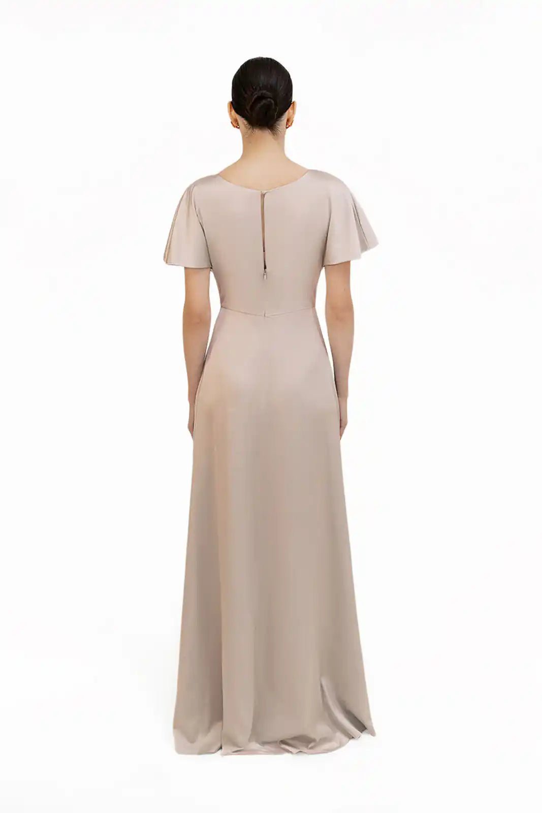 A woman faces away, wearing the TH&TH Camilla Bridesmaid Dress in Champagne Sky Satin with a twist-knot bodice, short flutter sleeves, and a keyhole back, set against a plain white backdrop.