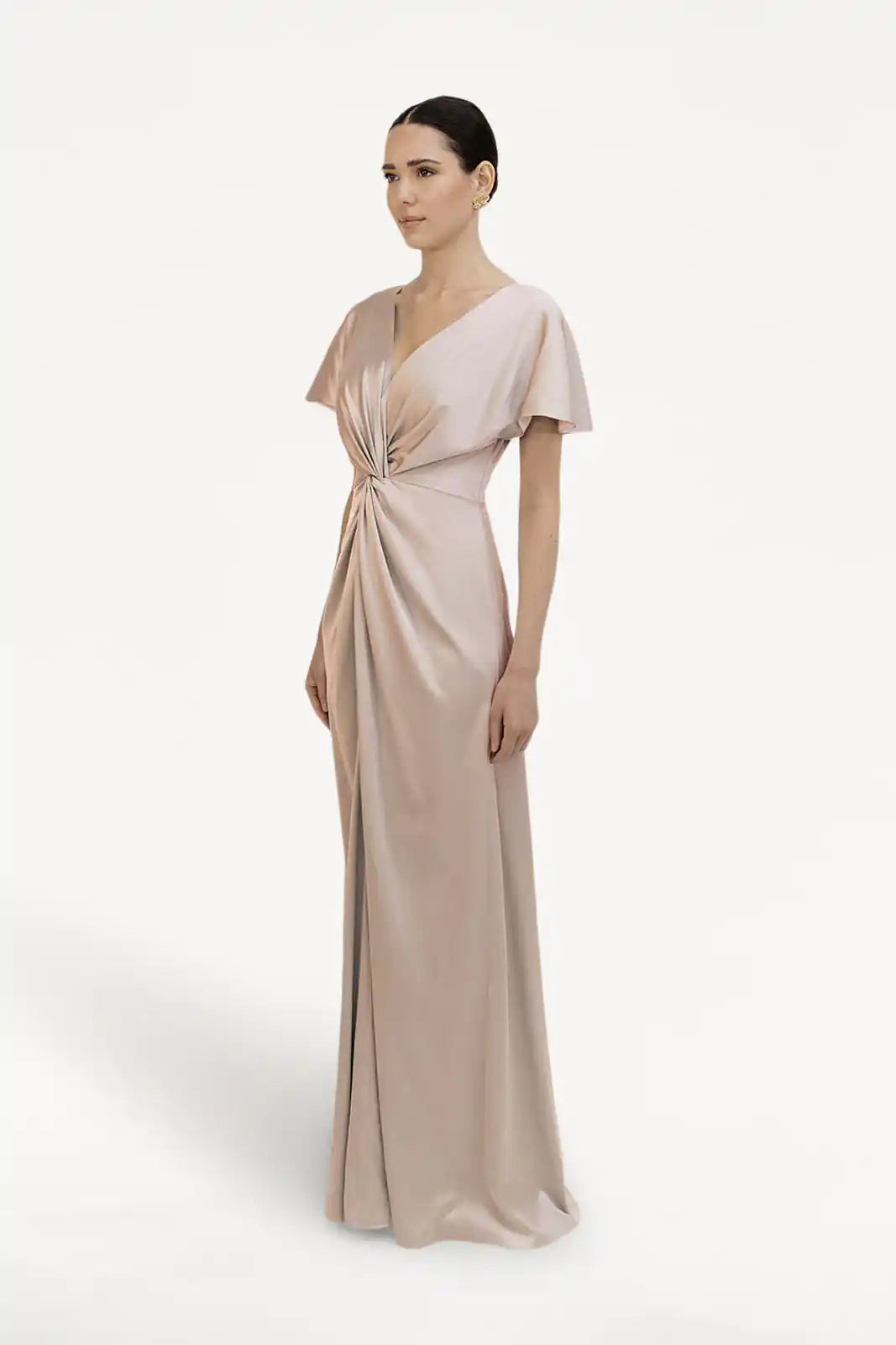 Woman stands in the Camilla Bridesmaid Dress by TH&TH, featuring size-inclusive design, short sleeves, twist-knot waist, and champagne sky satin fabric against a plain white background.