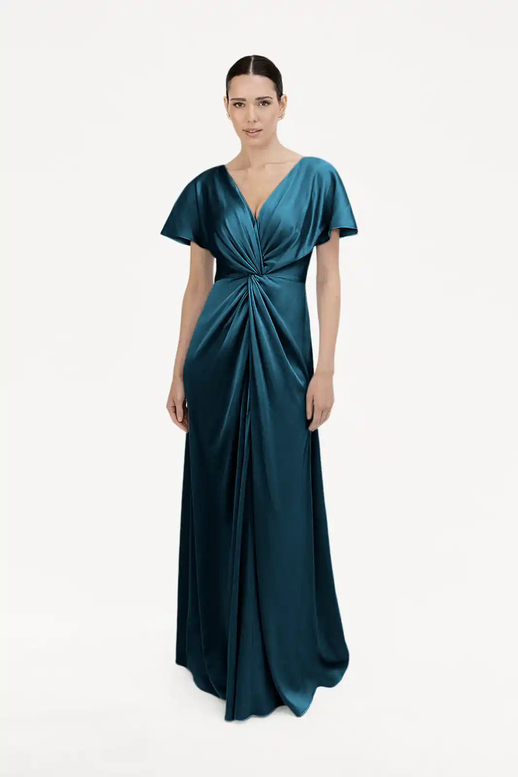 A woman models the Camilla Bridesmaid Dress in Emerald Dawn Satin by TH&TH, a floor-length gown featuring short sleeves, a deep V-neckline, and a gathered twist waist detail, set against a plain white background.