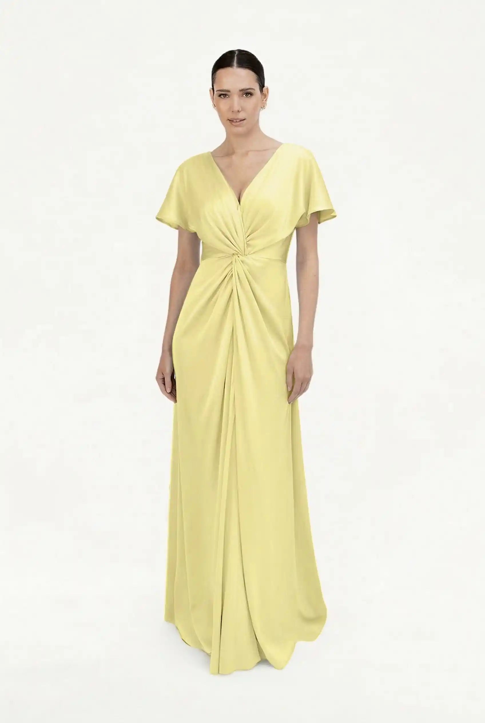 A woman stands against a white background wearing the TH&TH Camilla Bridesmaid Dress in Limoncello Satin—a size-inclusive, floor-length gown featuring short flutter sleeves, a deep V-neck, and gathered draping at the waist.