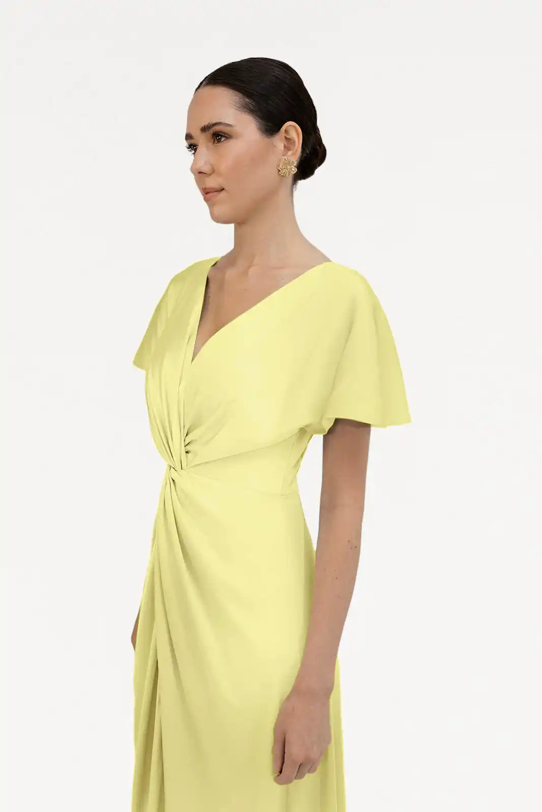 A woman with dark hair in a low bun models the TH&TH Camilla Bridesmaid Dress in Limoncello Satin, featuring a size-inclusive fit, short sleeves, V-neck, and twist-knot waist detail, against a plain white background.