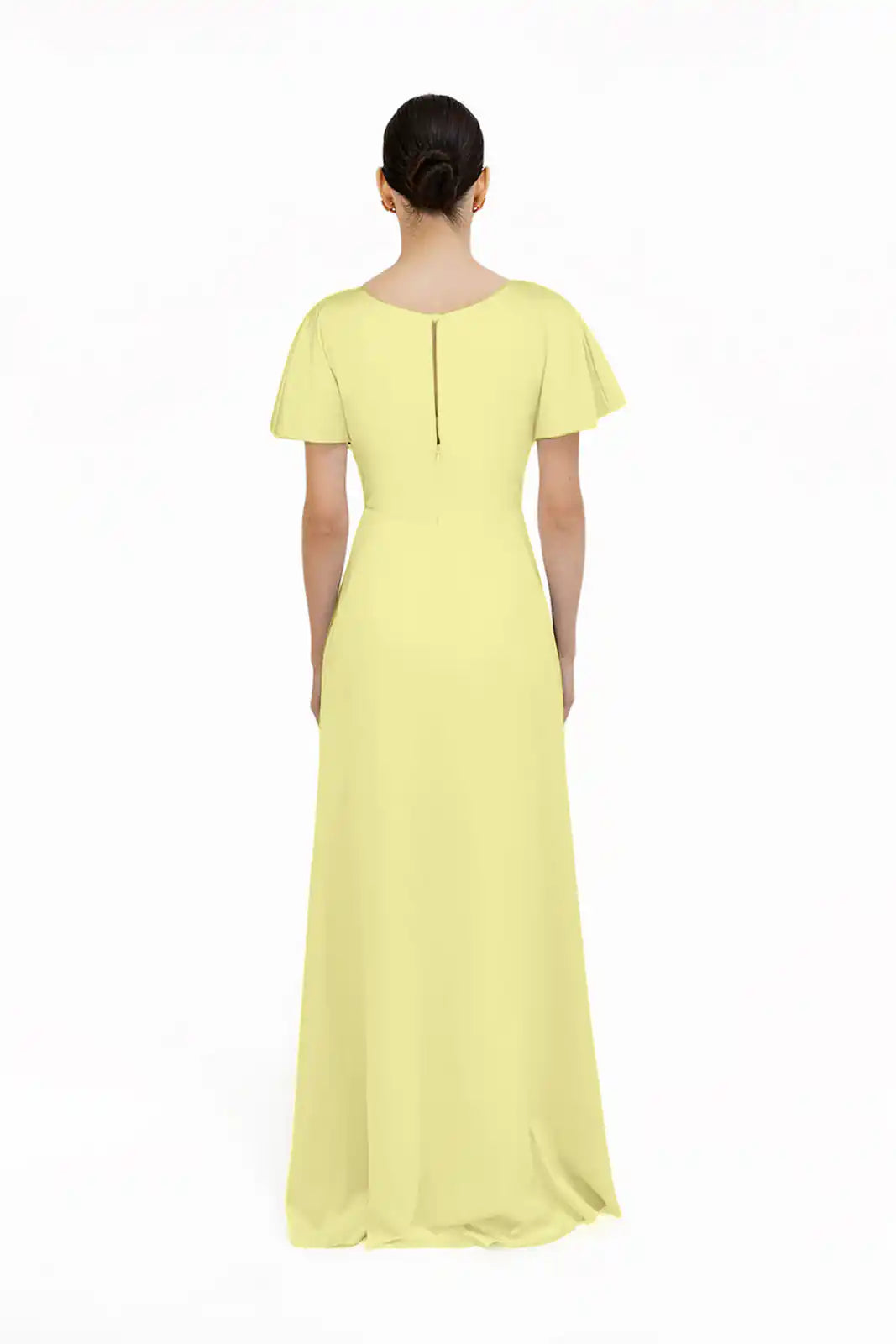 A woman faces away, wearing the floor-length Camilla Bridesmaid Dress in Limoncello Satin by TH&TH. Her hair is styled in a low bun against a plain white background.
