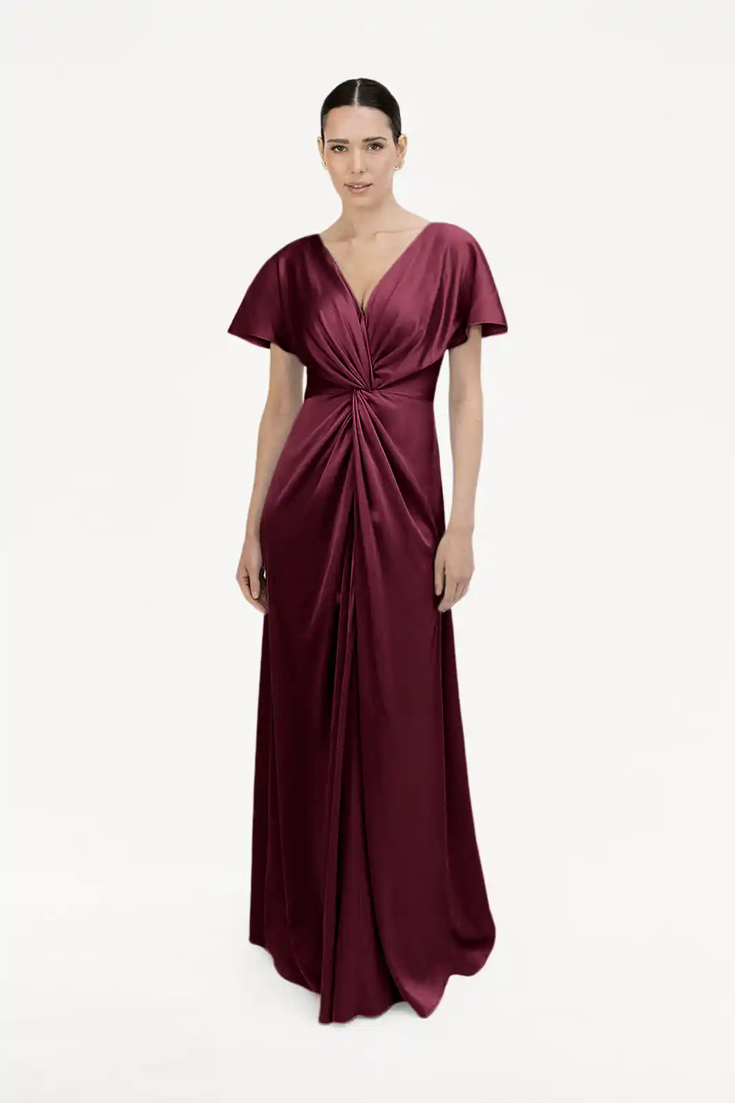 A woman wears the TH&TH Camilla Bridesmaid Dress in Merlot Satin, featuring a floor-length silhouette, short sleeves, V-neckline, and gathered twist waist detail—all set against a plain white background.