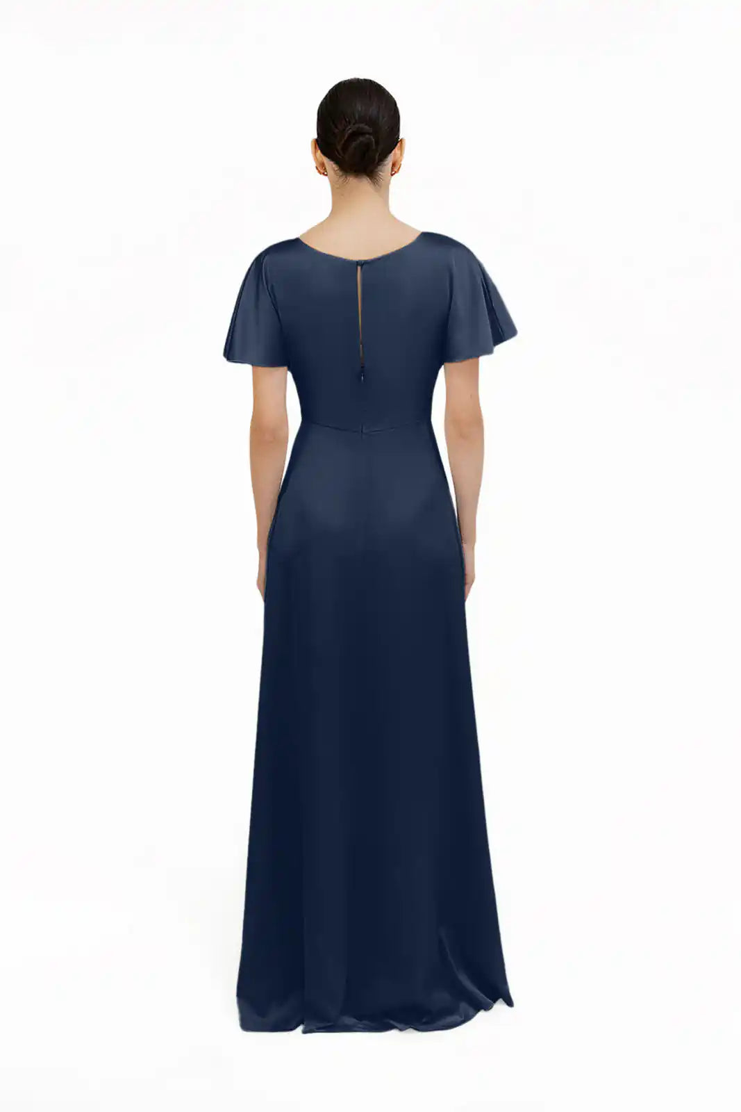 A woman, seen from behind, wears the size-inclusive Camilla Bridesmaid Dress in Navy Satin by TH&TH. The floor-length gown features short sleeves, a fitted waist, back zipper, and subtle sheen, styled simply against a plain white background.