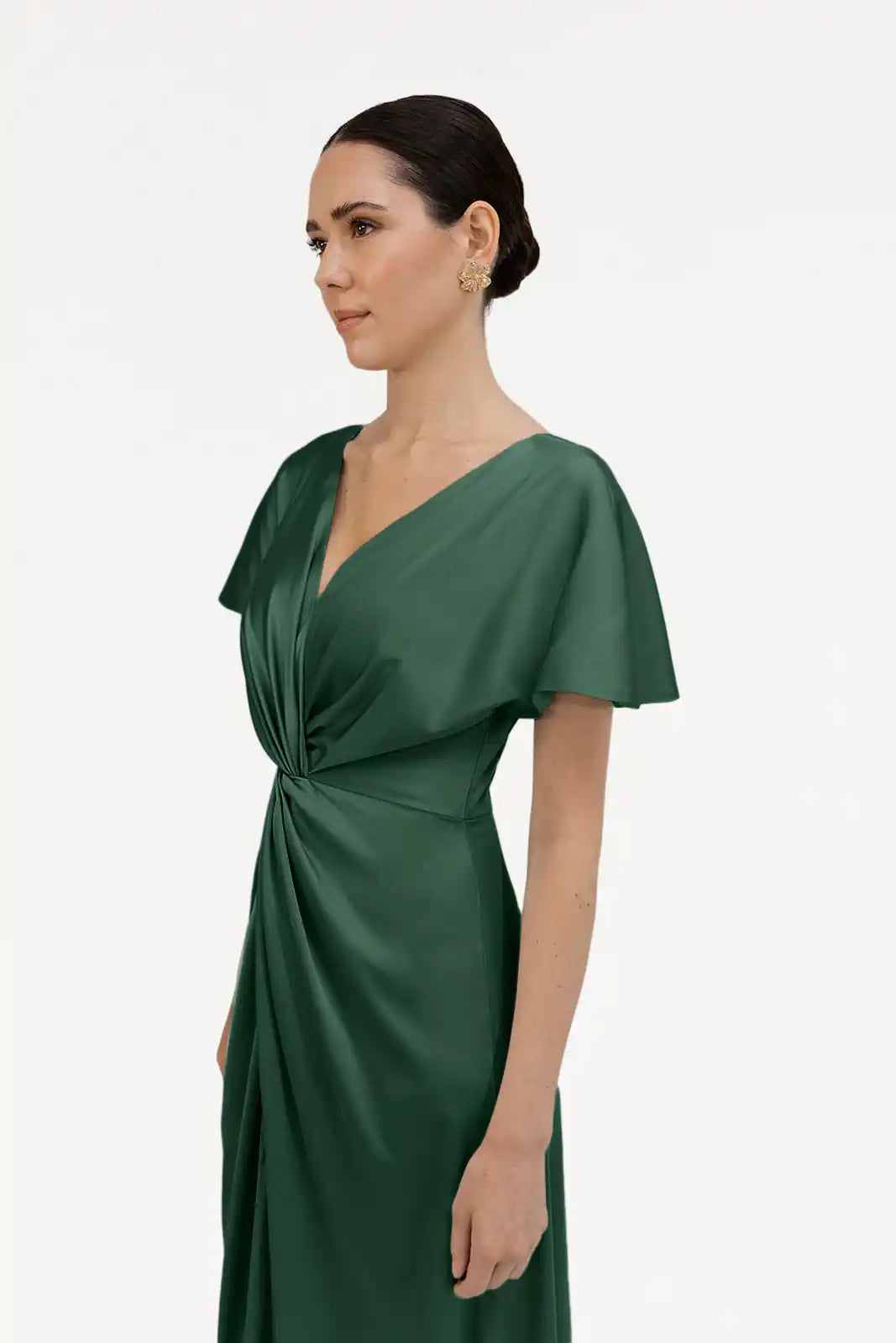 A woman with dark hair styled back wears the Camilla Bridesmaid Dress in Olive Grove Satin by TH&TH, featuring short sleeves, a V-neck, and a twisted knot waist detail, standing against a plain white background.