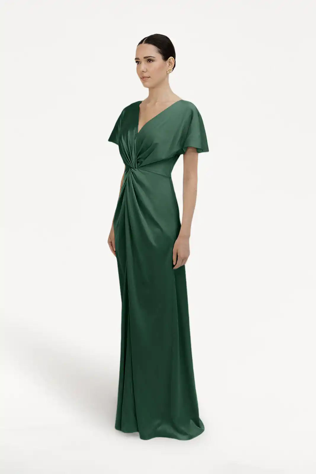 A woman models the TH&TH Camilla Bridesmaid Dress in Olive Grove Satin—a green, floor-length gown with short sleeves, a V-neckline, and a gathered twist waist—posed against a plain white background.